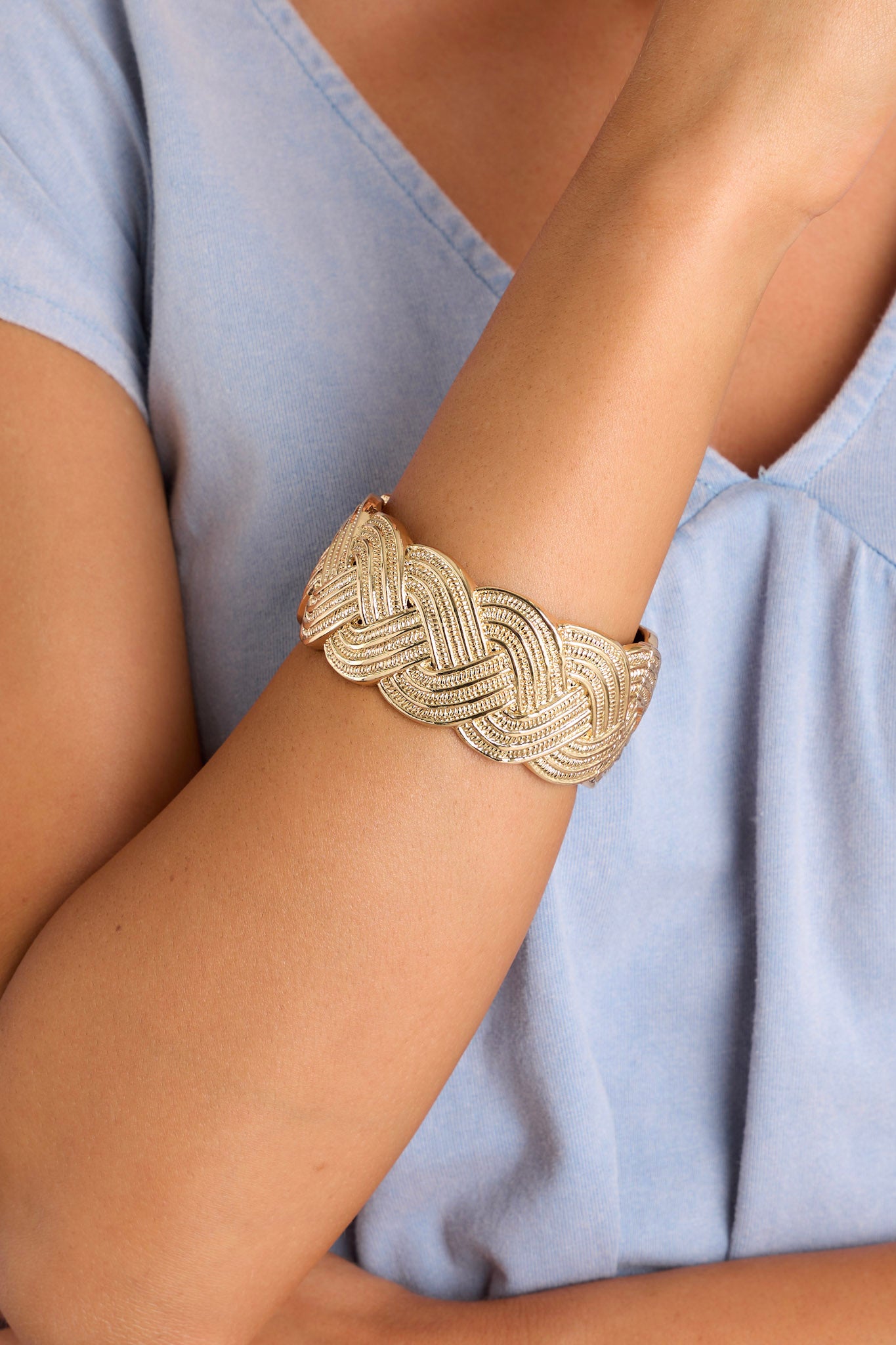 Close-up of this gold cuff that features a wide band, a textured braided design, and a spring hinged closure.