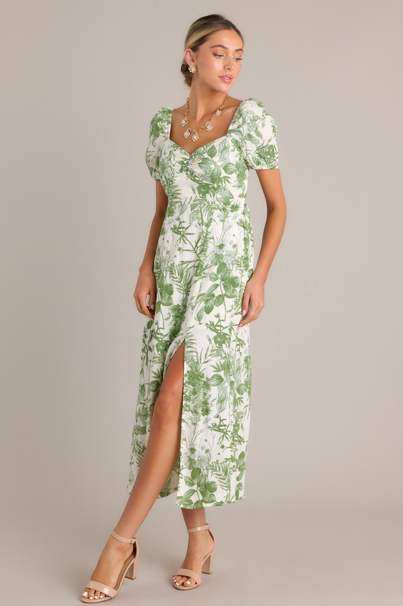 This green floral midi dress features short puff sleeves, a sweetheart neckline, a fitted bodice, a cinched waist, and a mid-length skirt with a front slit.