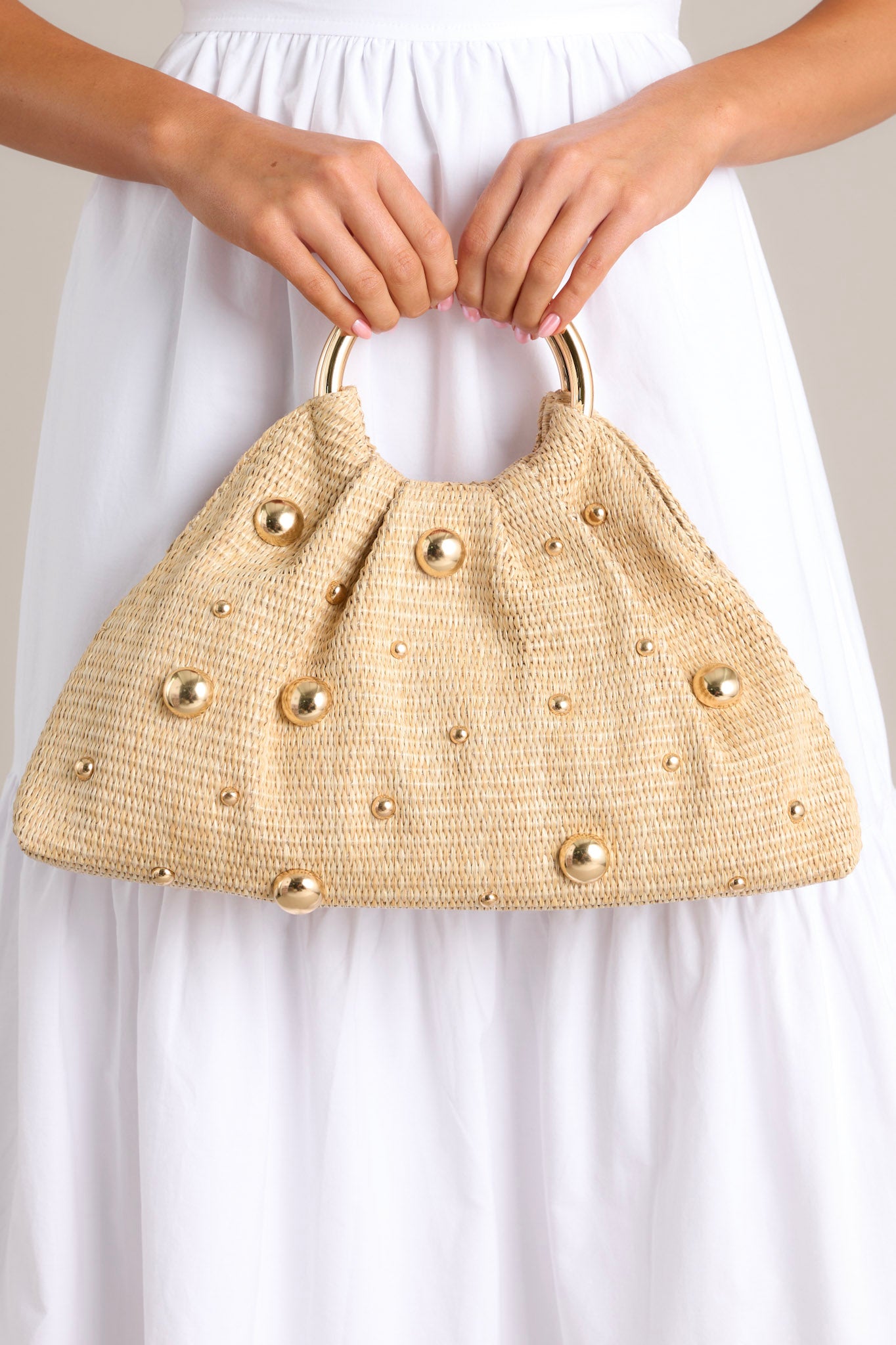 Front view of this rattan clutch that features round shiny gold handles, a magnetic closure, a spacious interior with a smaller pocket inside, and round shiny gold embellishments that vary in size.