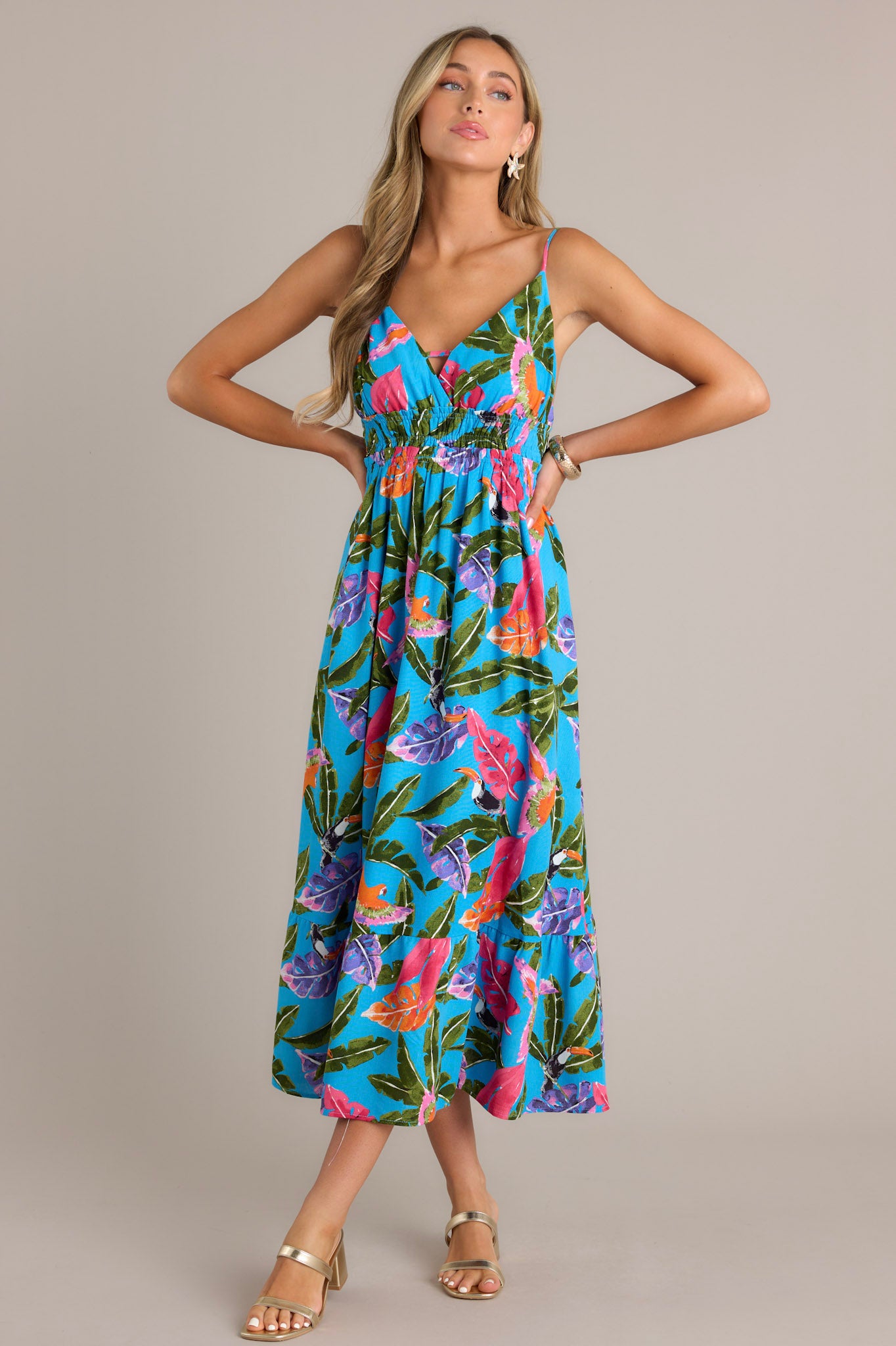 Full length view of a blue midi dress featuring a V-neckline, thin adjustable straps, an open back, smocked waistband, and a flowing silhouette.