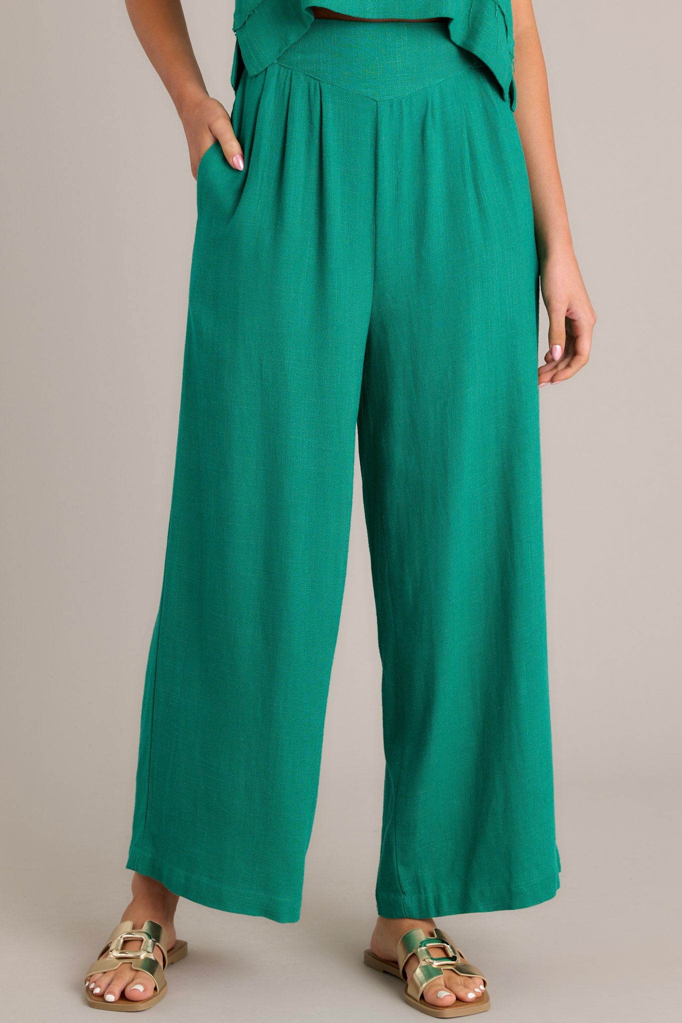 Front view of high-waisted green pants featuring an elastic insert in the back, functional hip pockets, lightweight fabric, and a wide leg design.