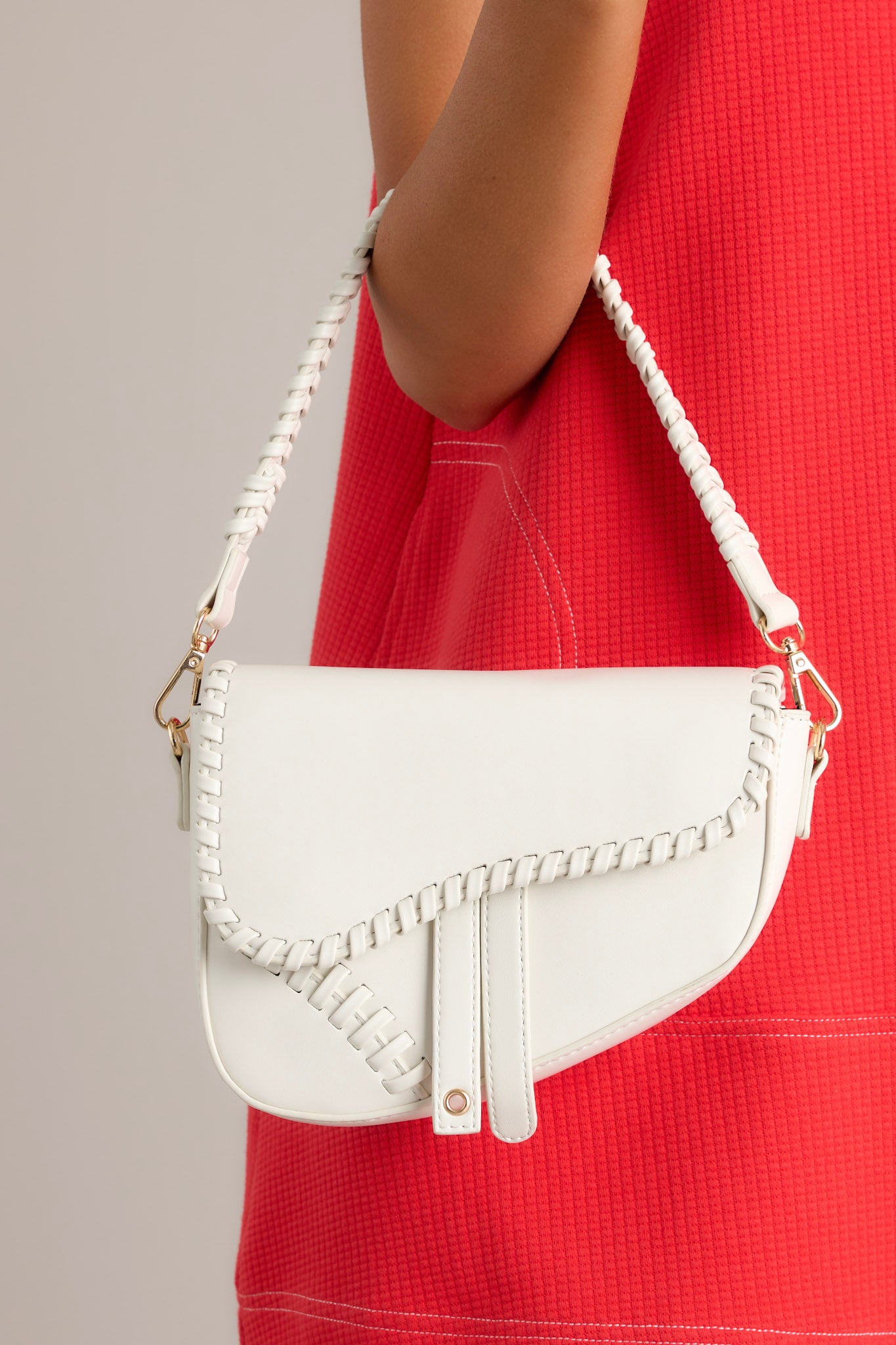 This white handbag features gold hardware, faux leather, a braided strap, a magnetic snap closure, a zipper pocket inside, and an additional strap.