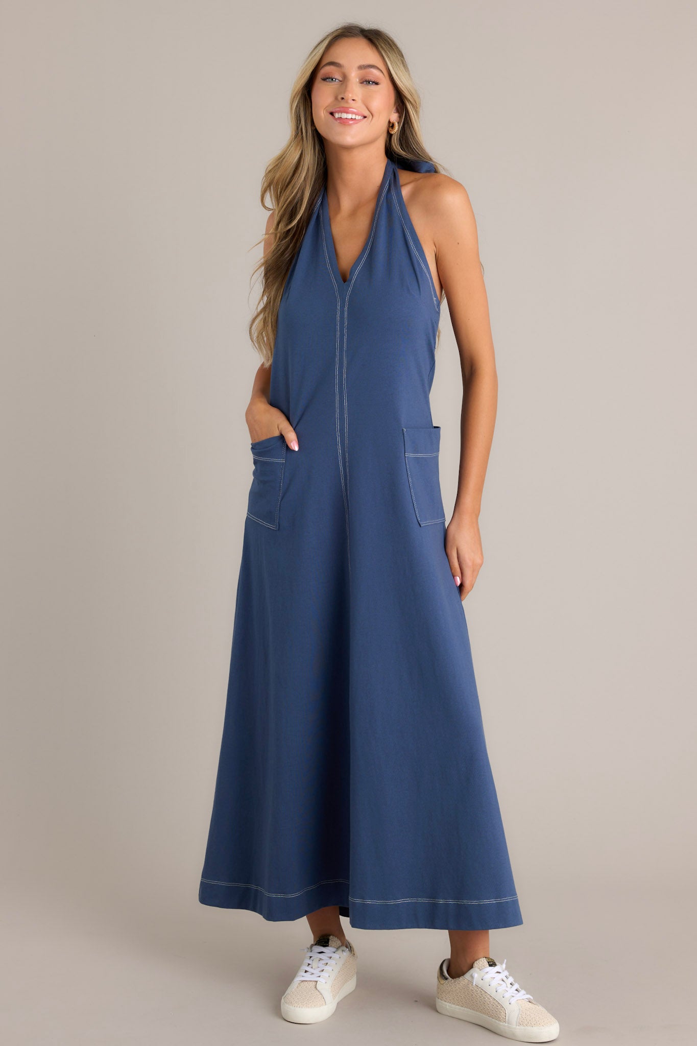 Long blue dress with a halter neckline, deep V-front, and practical patch pockets.