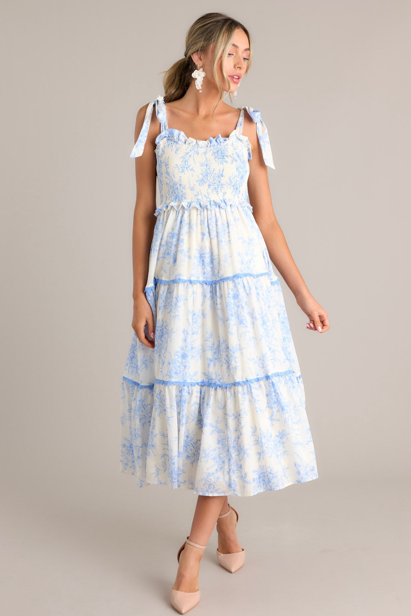 Angled view of this light blue midi dress that features a ruffled sweetheart neckline, self-tie straps, a fully smocked bodice, functional hip pockets, and scalloped tiers.