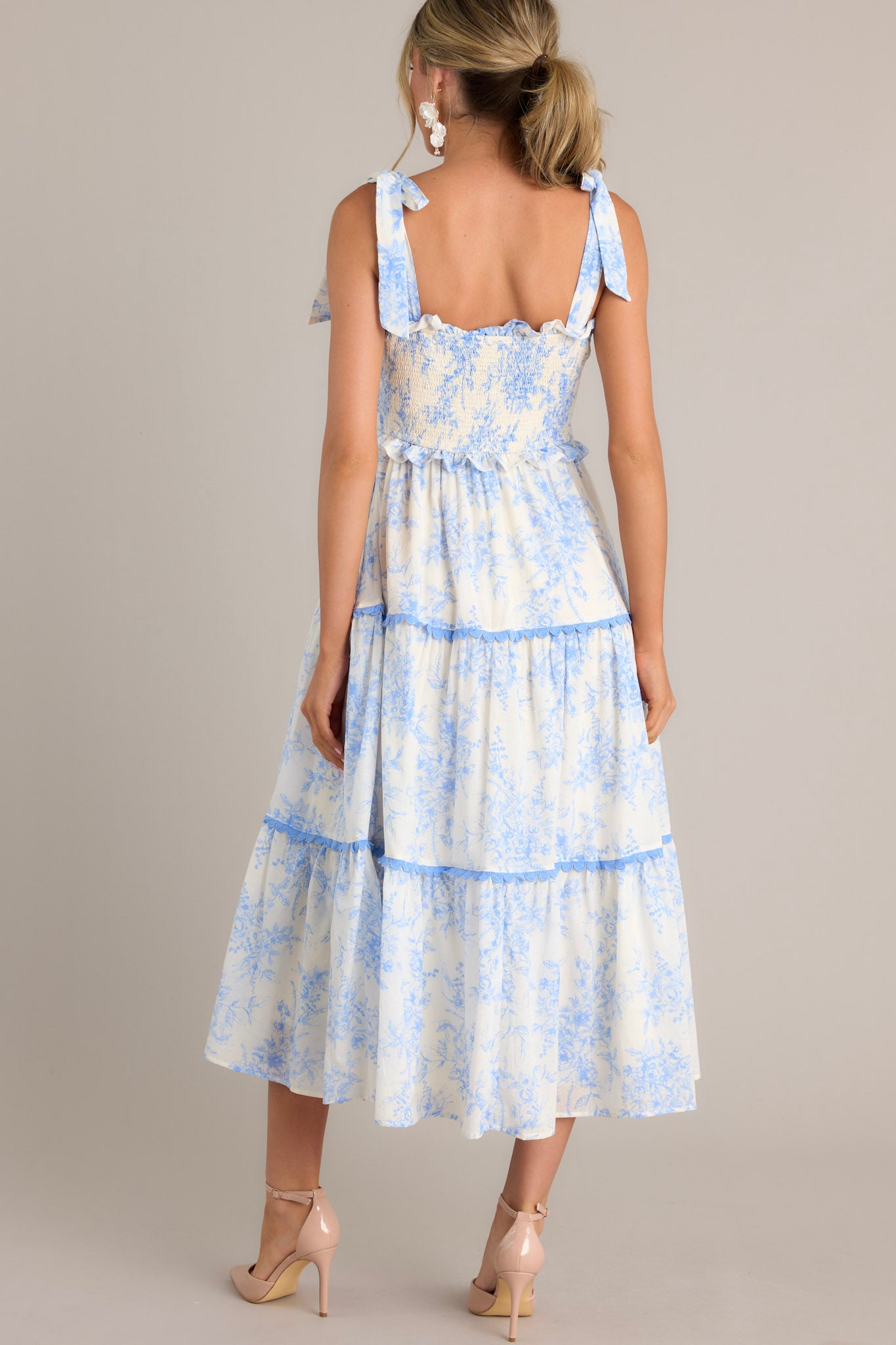 Back view of this light blue midi dress that features a ruffled sweetheart neckline, self-tie straps, a fully smocked bodice, functional hip pockets, and scalloped tiers.