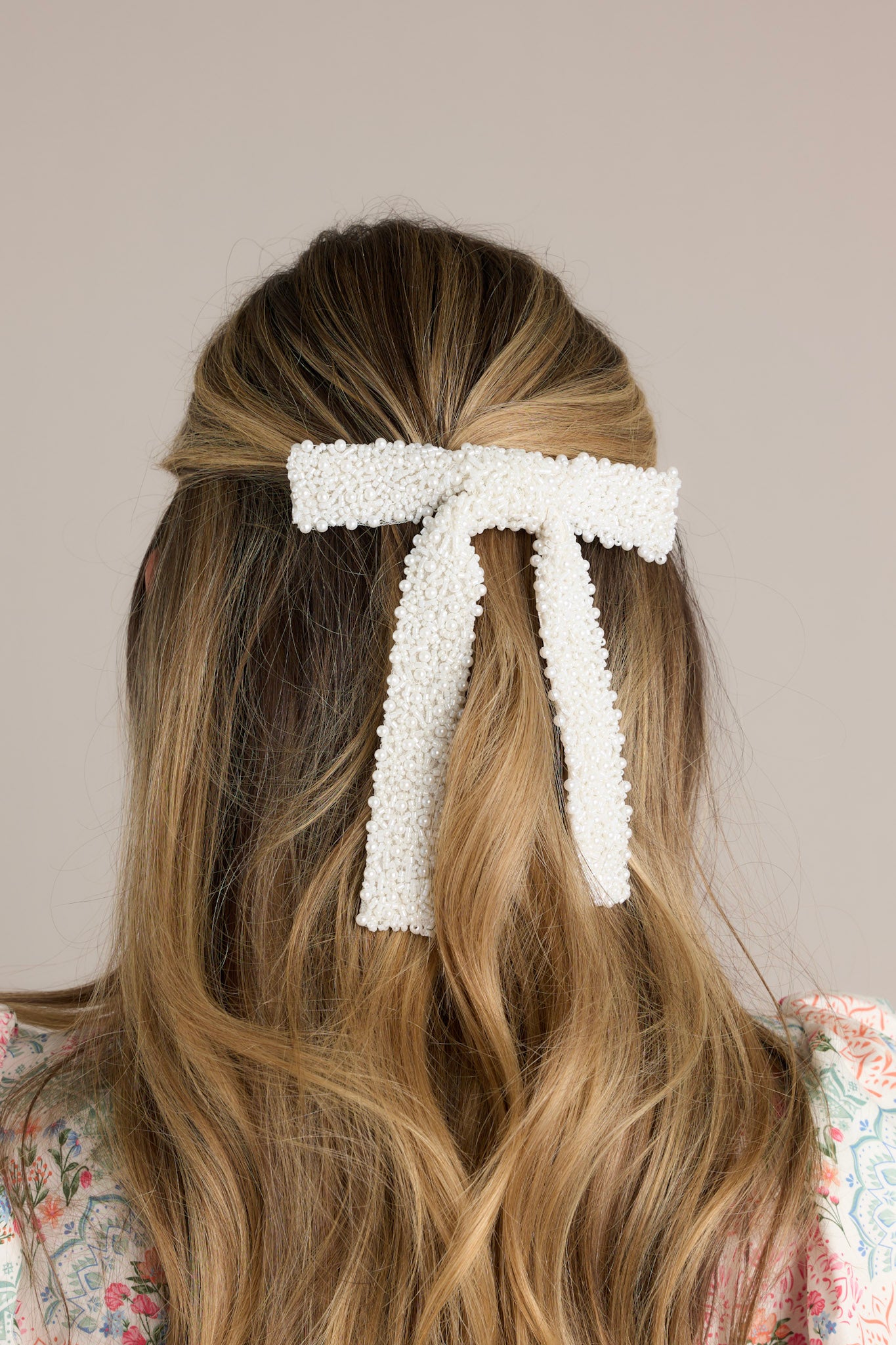 Close up view of this pearl beaded bow that features a beaded faux pearl detailing and a silver french style barrette.