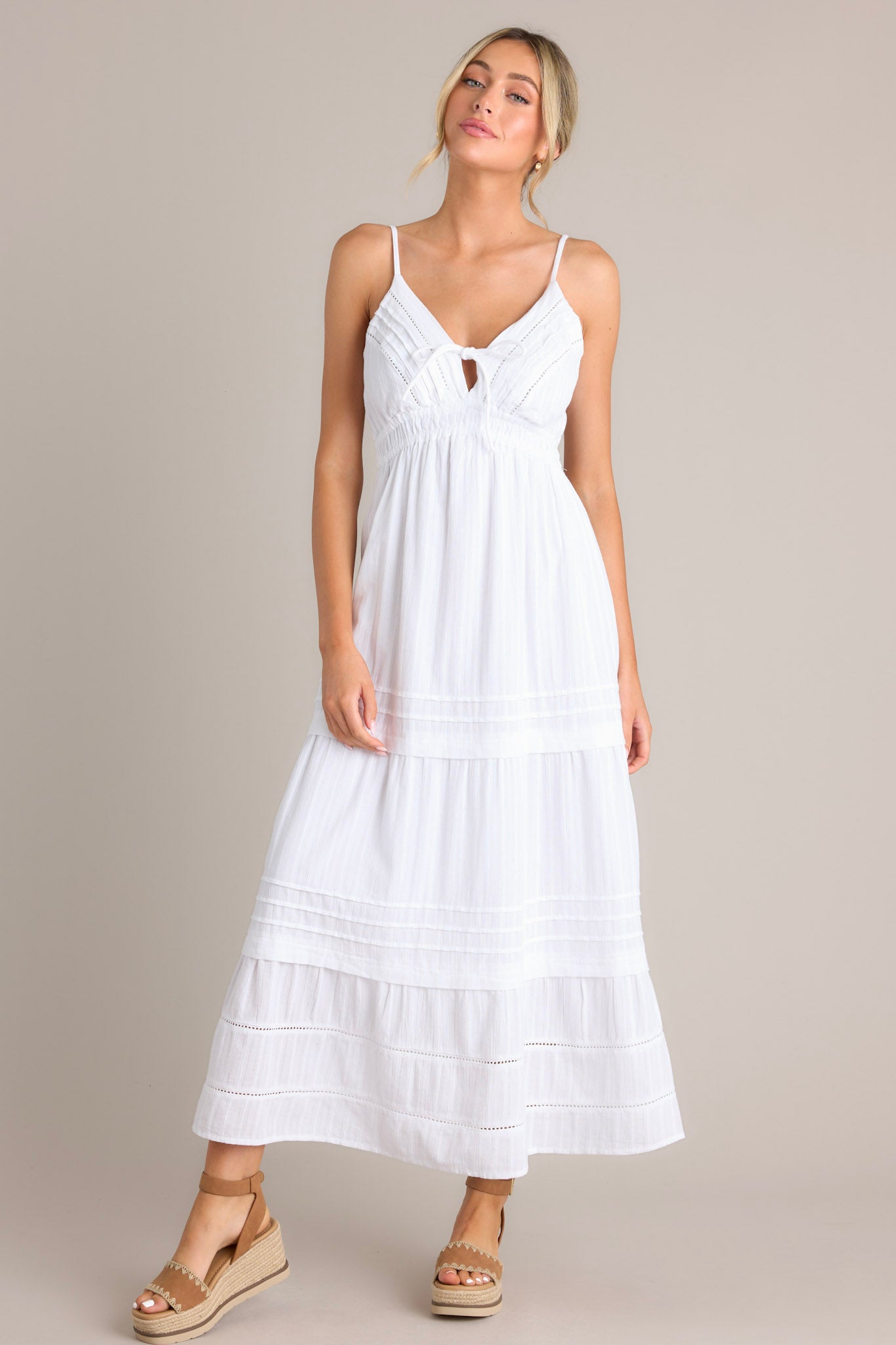 Front view of this white midi dress that features a v-neckline, thin adjustable straps, eyelet bust detailing, a self-tie bust feature, an elastic waistline, and a tiered design.