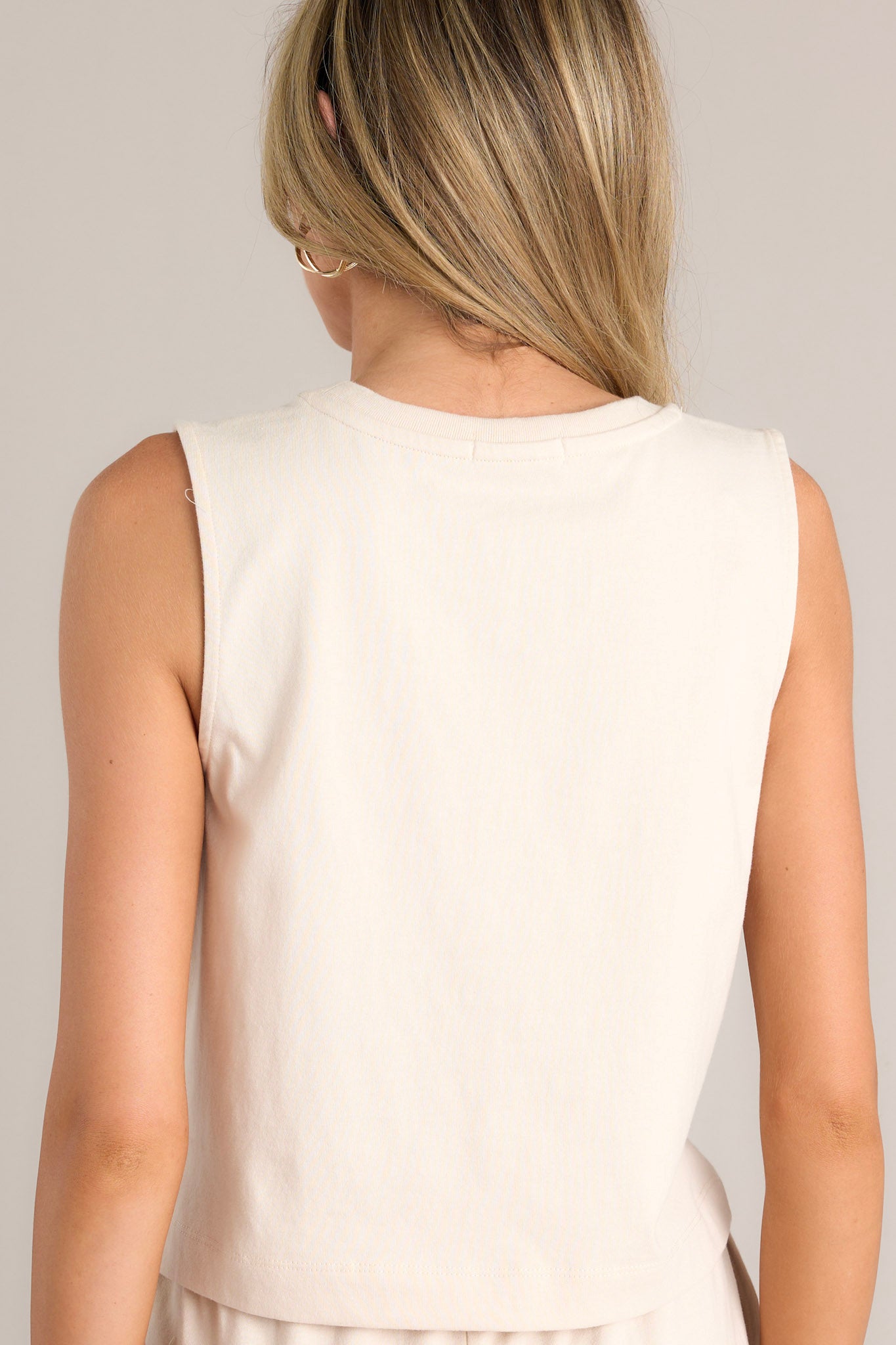 Back view of this sandshell jersey tank that features a ribbed scoop neckline, a wide sleeve, a high back, and a cropped design.