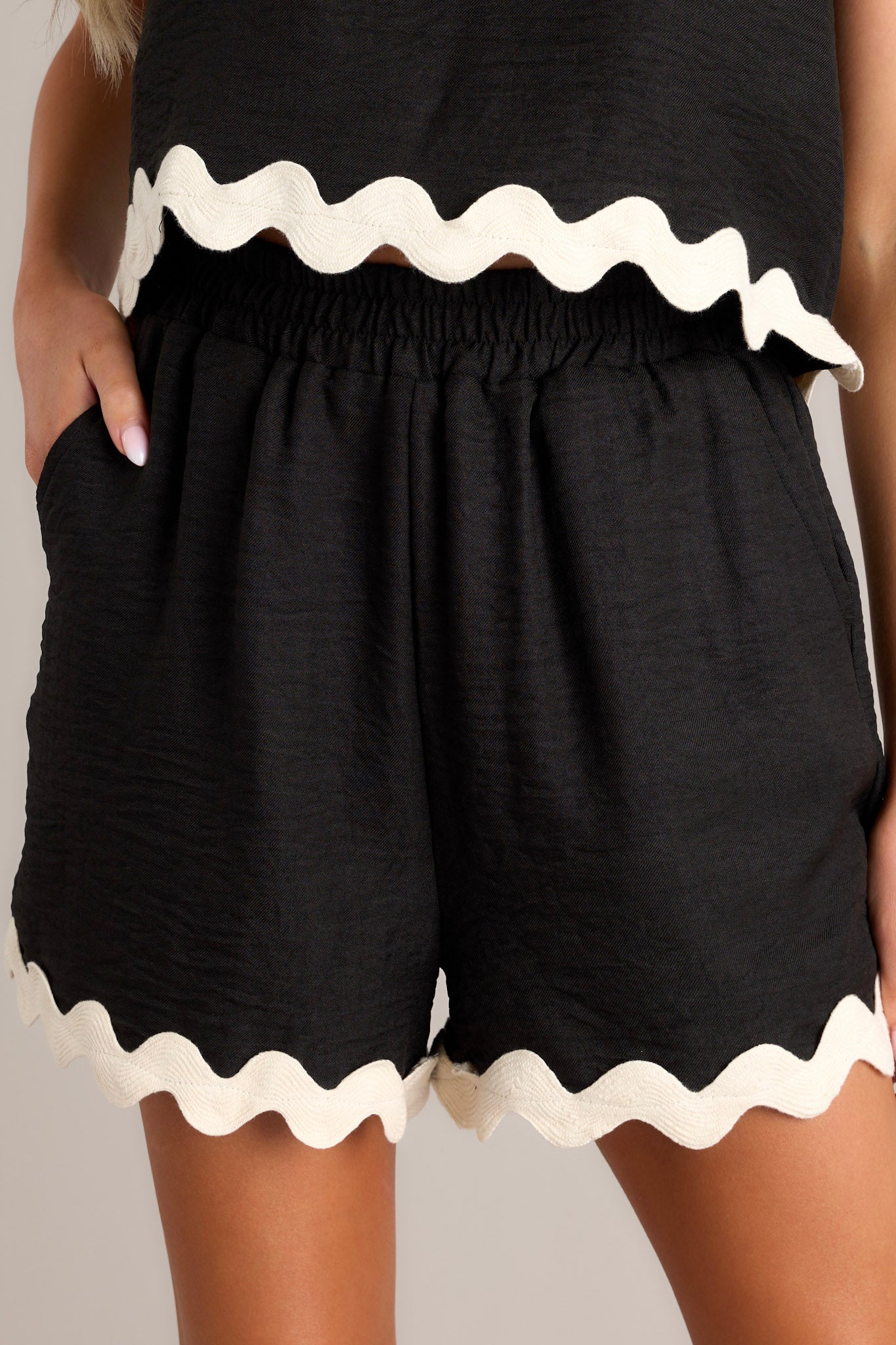 These black shorts feature a mid-rise smocked elastic waistband, pockets at the hips, and a scalloped hem.