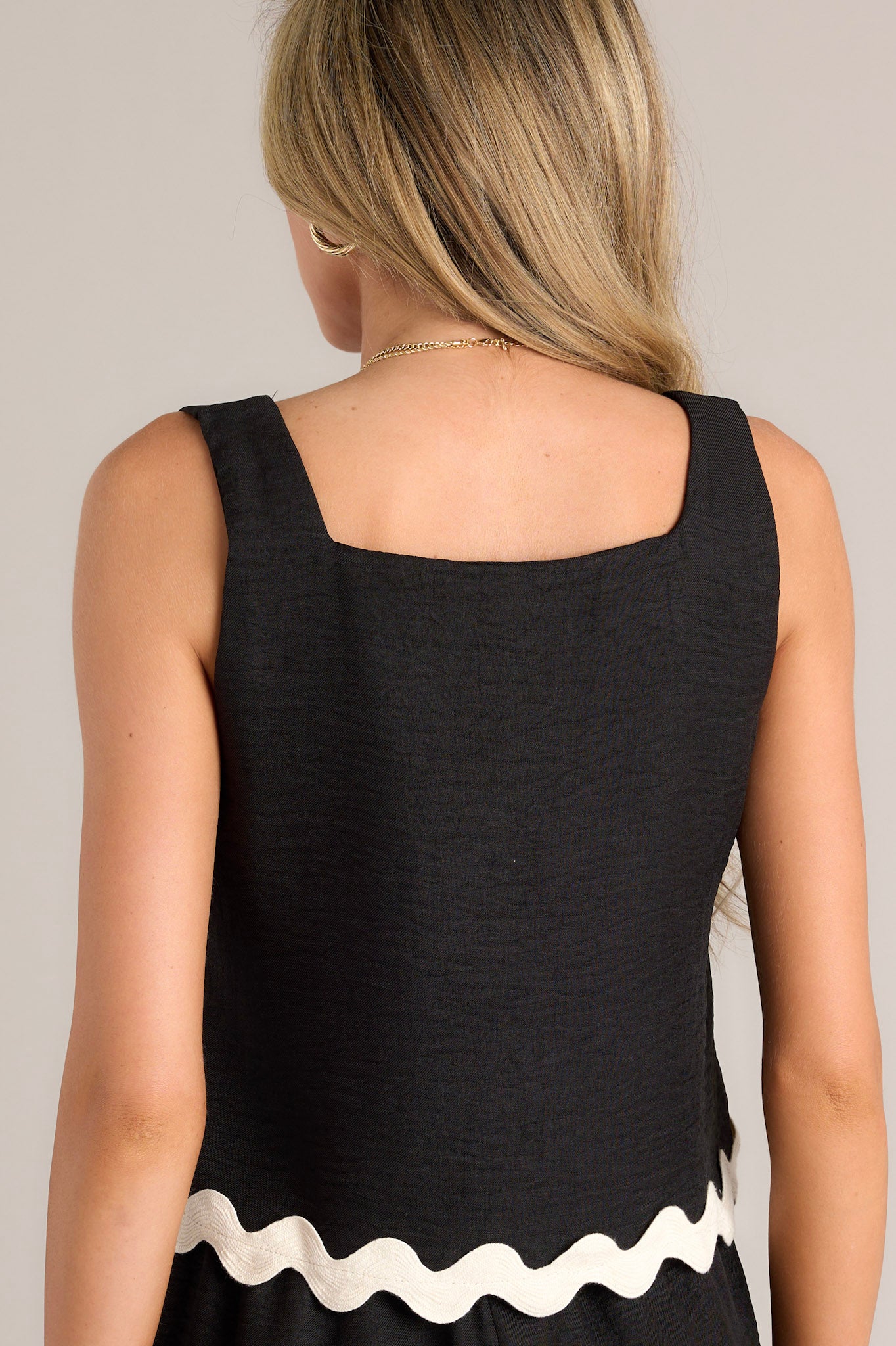 Back  view of this black tank top that features a square neckline, wide straps, a boxy fit, and a scalloped detail at the hem.