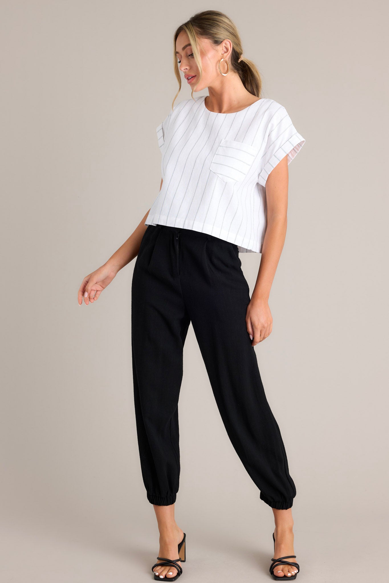 Angled full body view of this white top that features a crew neckline, functional buttons down the back, a functional breast pocket, cuffed wide short sleeves, and a cropped hemline.