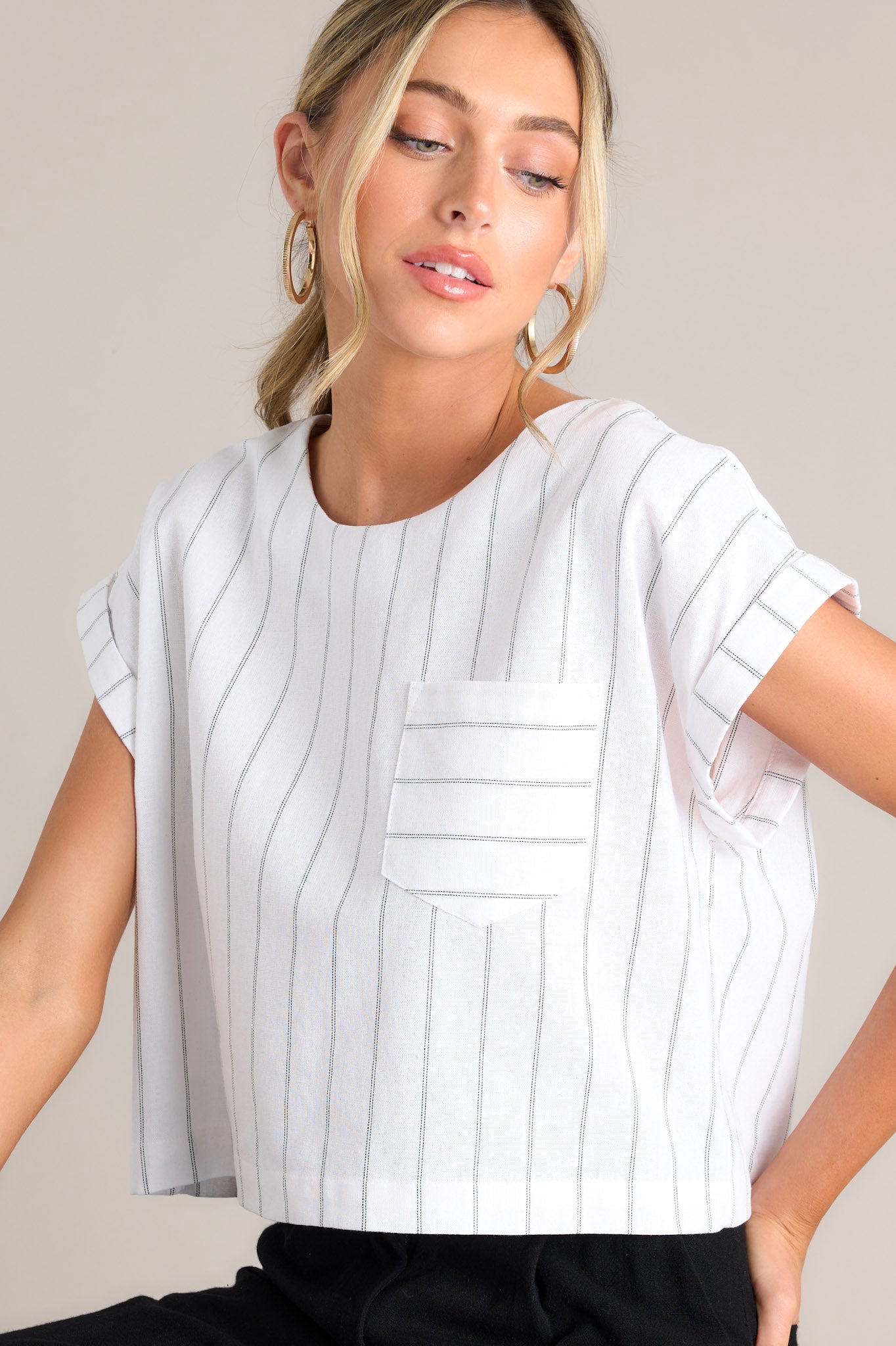 Side view this white top that features a crew neckline, functional buttons down the back, a functional breast pocket, cuffed wide short sleeves, and a cropped hemline.