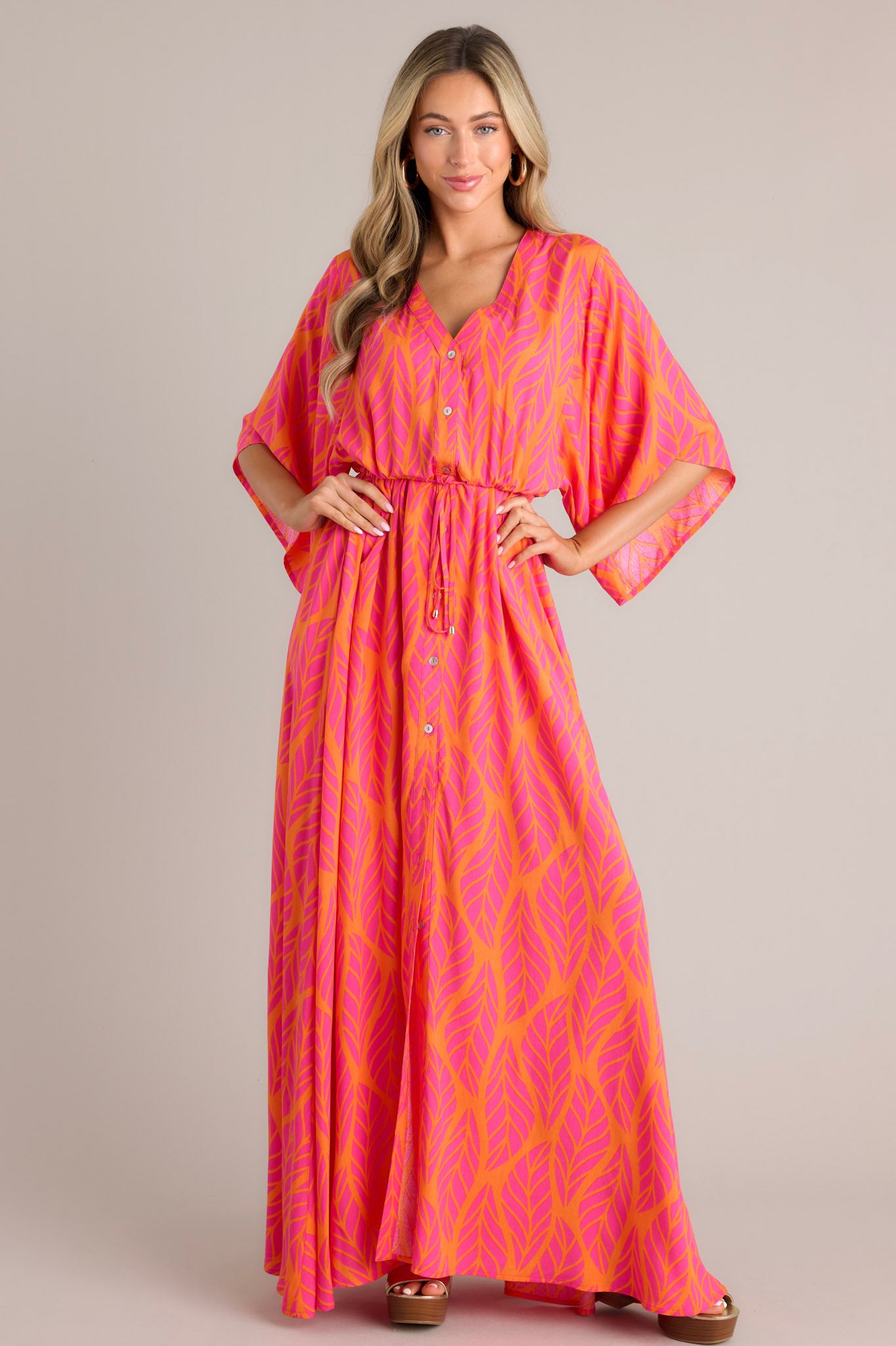 Front view of this hot pink maxi dress that features a v-neckline, a functional button front, a self-tie drawstring waist, a flowing silhouette, and flowing half sleeves.