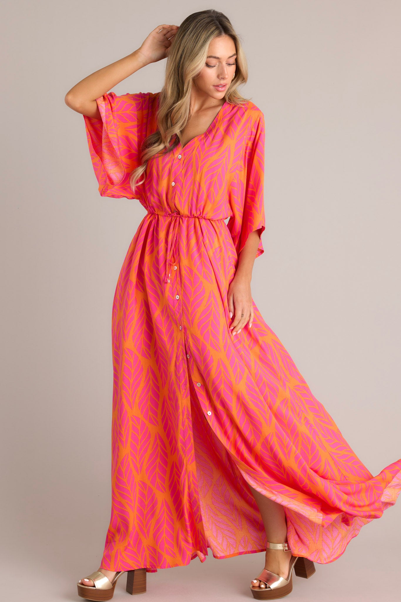 Side view of this hot pink maxi dress that features a v-neckline, a functional button front, a self-tie drawstring waist, a flowing silhouette, and flowing half sleeves.