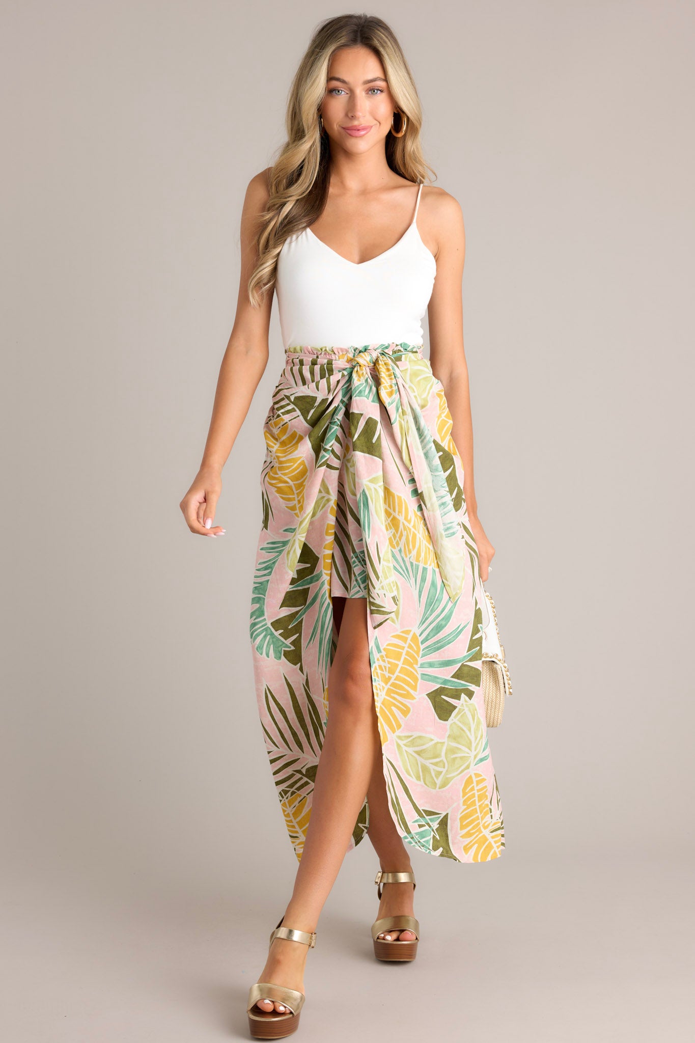 Full body view of this wrap skirt that features a high waisted design, an elastic waistband, a self-tie wrap feature that is positioned in the middle of the waistband, and a mini skirt underneath.