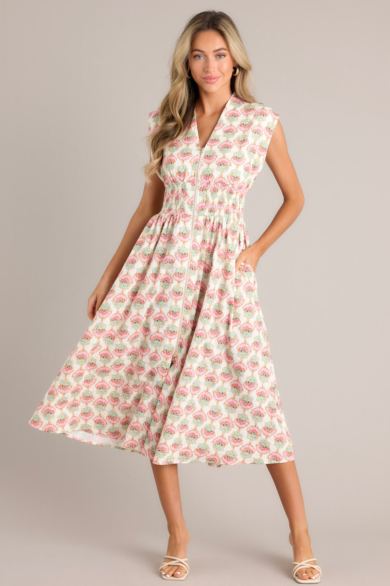 Front view of an ivory floral dress with a v-neckline, wide shoulders, a fully smocked waist, functional hip pockets, and a front slit.