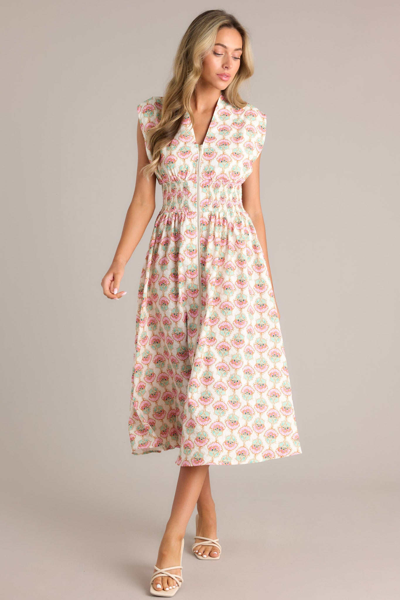 Full view of an ivory floral dress showcasing a v-neckline, wide shoulders, a full zipper front, and a fully smocked waist with functional hip pockets.