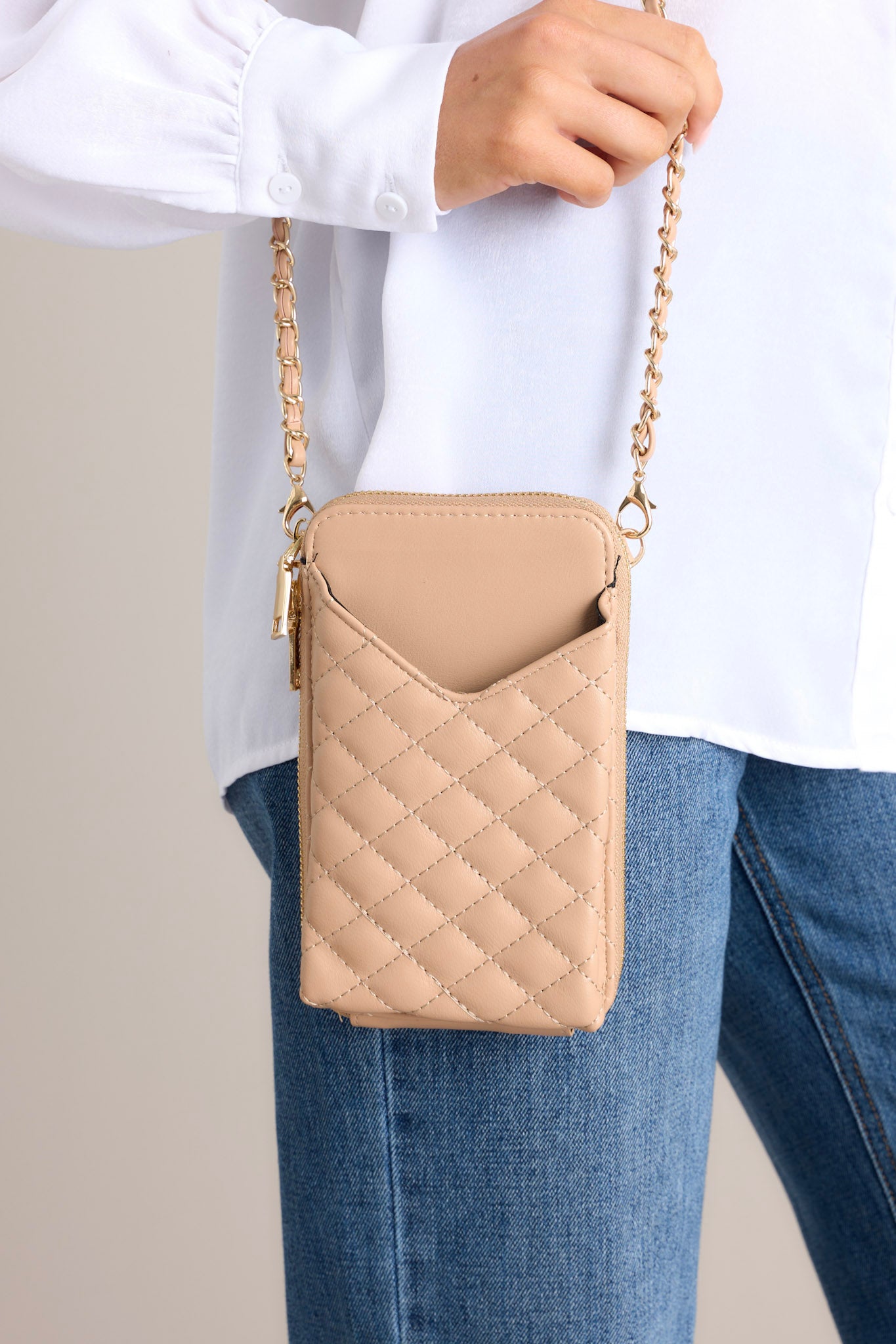 Close up of this tan, quilted, crossbody phone bag featuring gold hardware, a removable chain strap, a phone pocket, and multiple pockets inside.