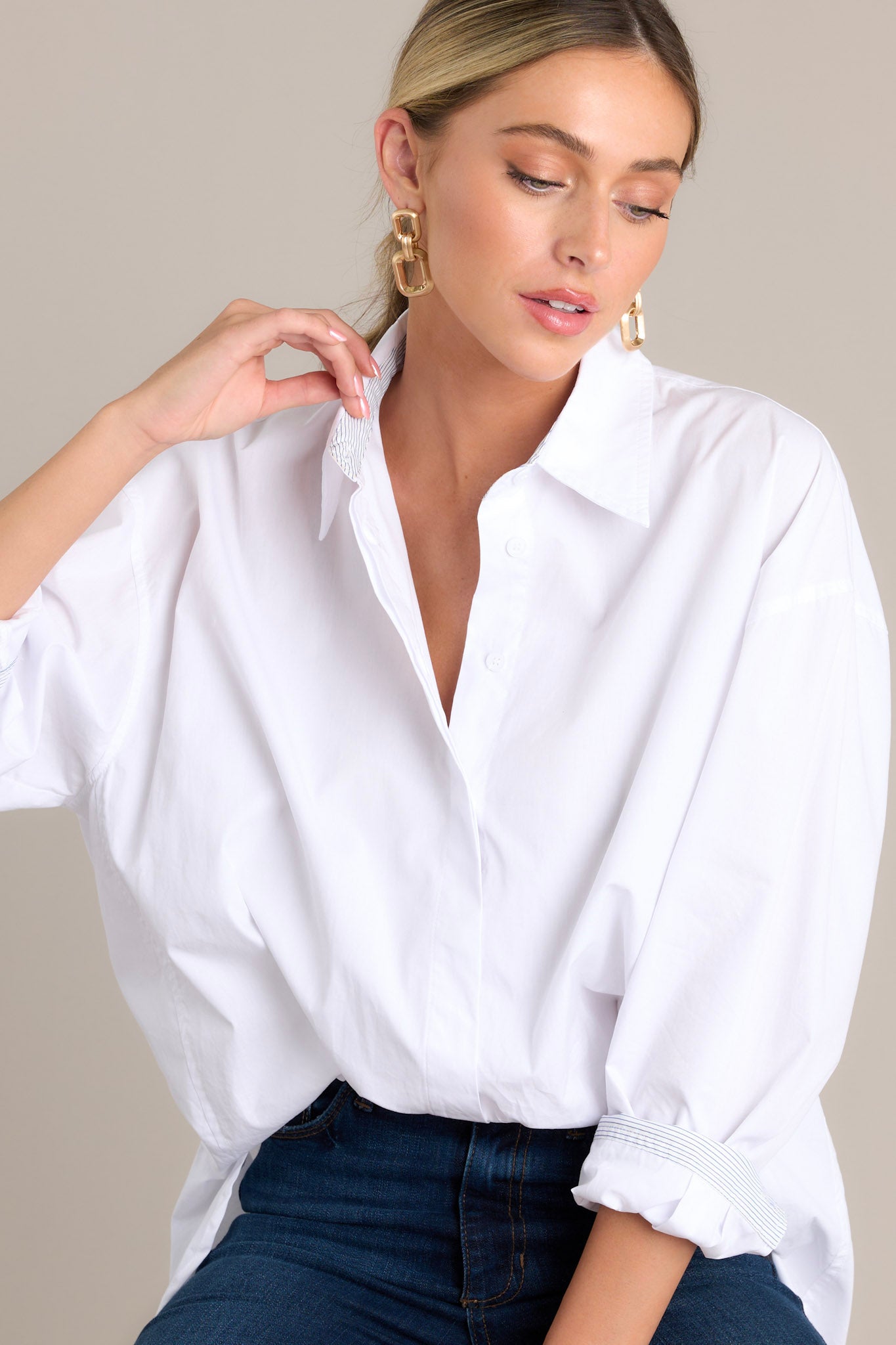 Seated Front angled view of a white top featuring a collared neckline, a full button front, striped button cuff sleeves, and a split scoop hemline