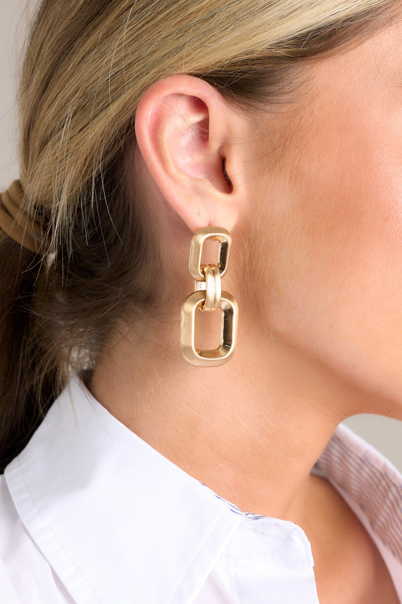 Close-up view of these gold earrings that feature two square links of different sizes, a matte and shiny finish, and secure post backings.