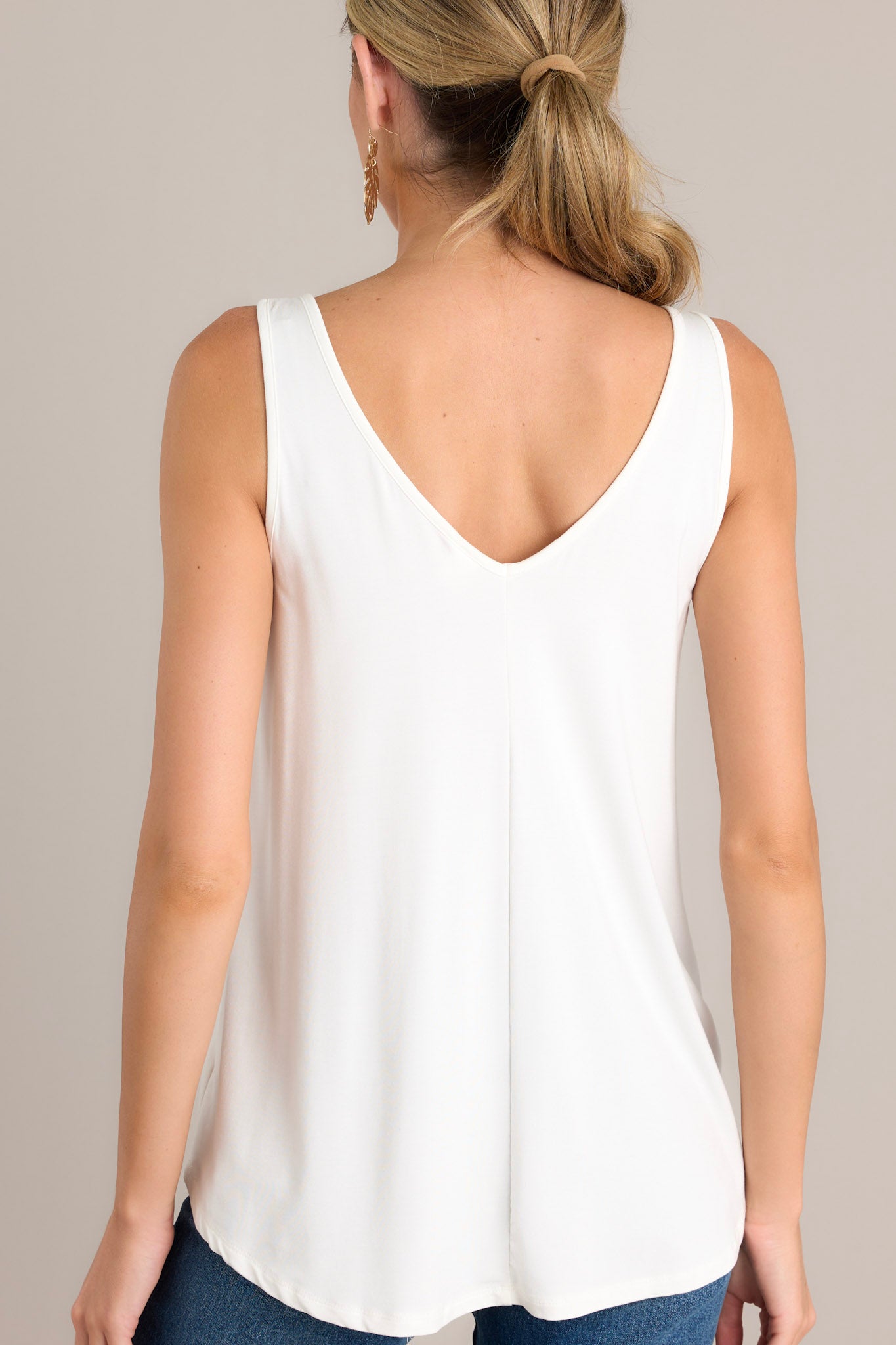 Back view of a white tank top highlighting the scoop bottom hem and the overall fit.