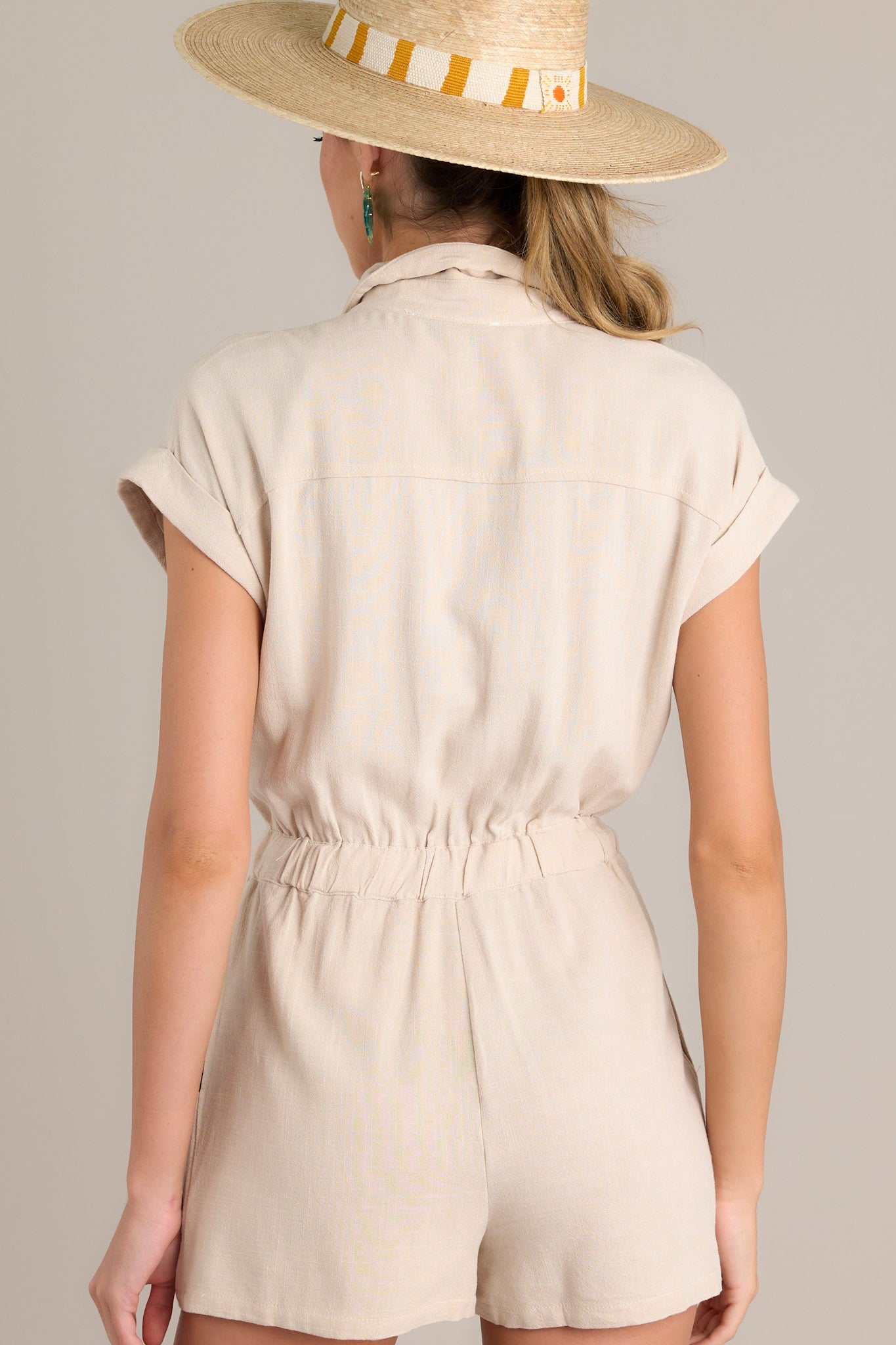 Rear view of the taupe romper highlighting the cuffed short sleeves and the back of the elastic waistband.