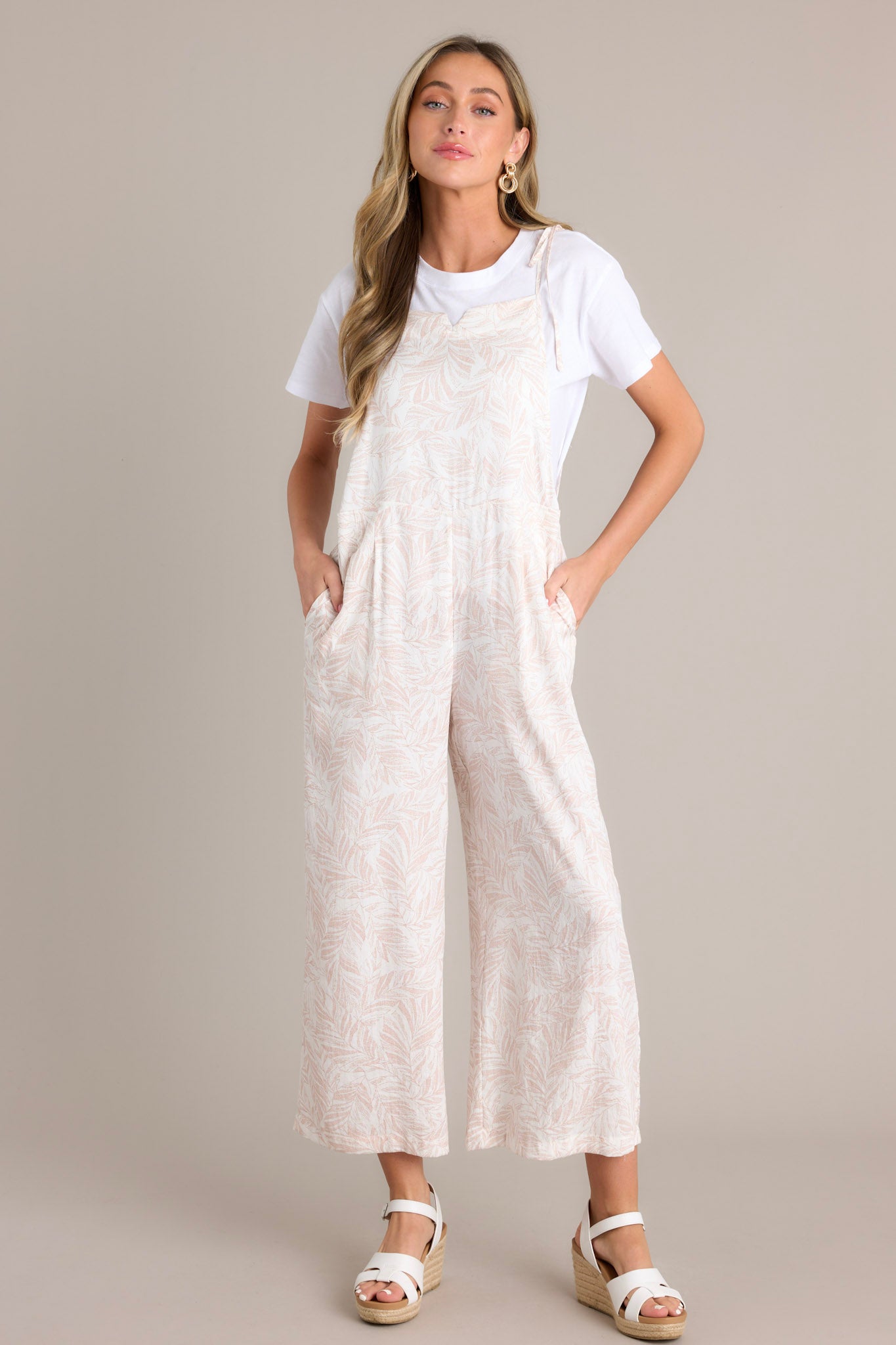 Full length view of natural overalls with a slitted square neckline, thin self-tie straps, functional hip pockets, and a wide leg design