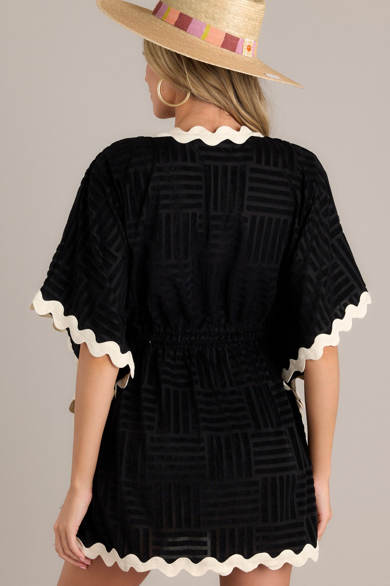 Back view of a black cover up highlighting the textured terry cloth design, contrasting ricrac trim, and wide flowing half sleeves.