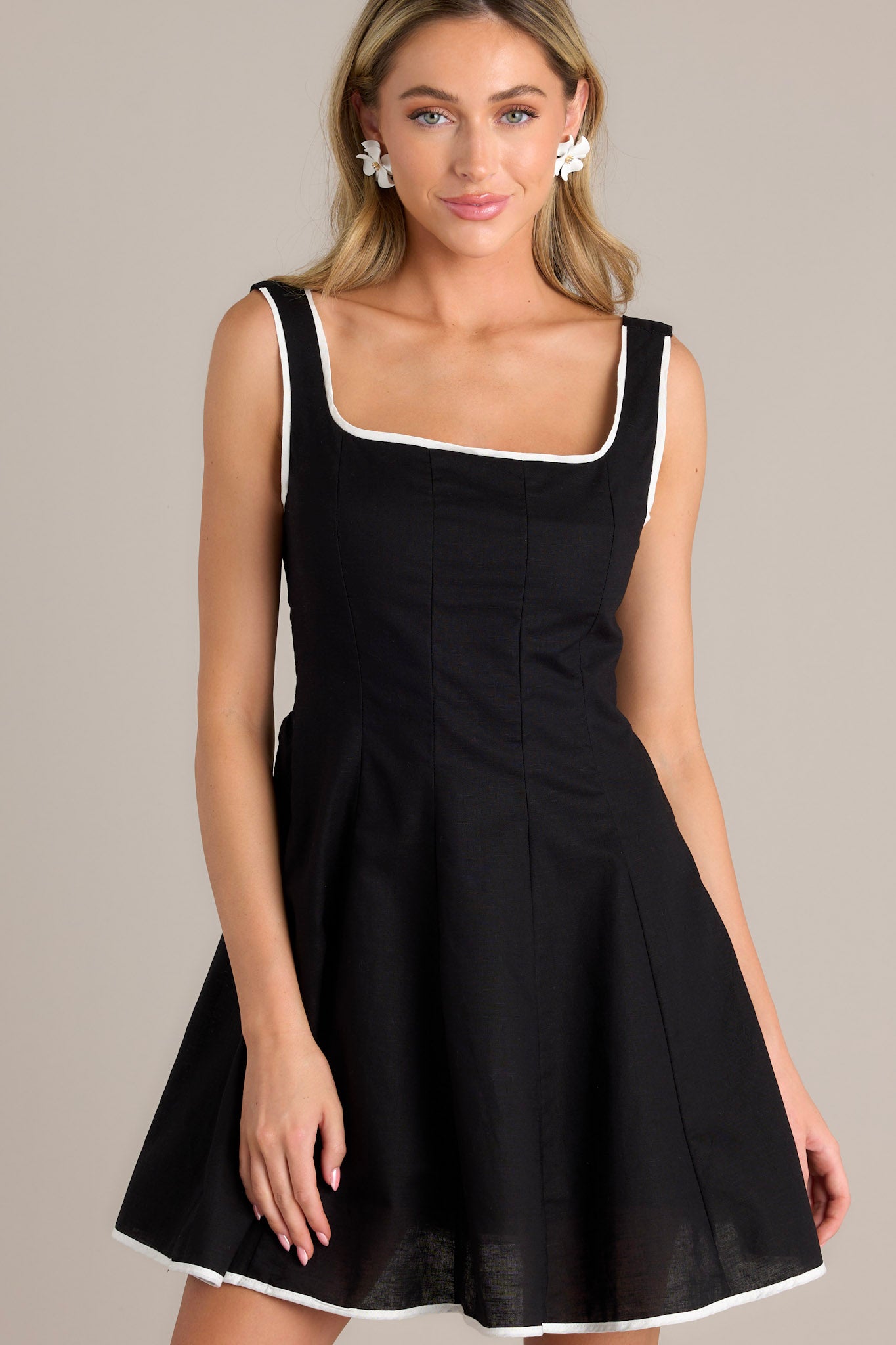 Full-length view of a black mini dress with thick adjustable straps, a square neckline, and white trim, styled with a smocked back insert and side zipper for a seamless look.