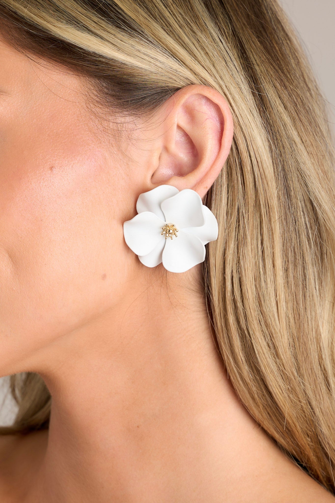 Close-up view of these white earrings that feature gold hardware, white flowers with defined petals, and secure post backings.