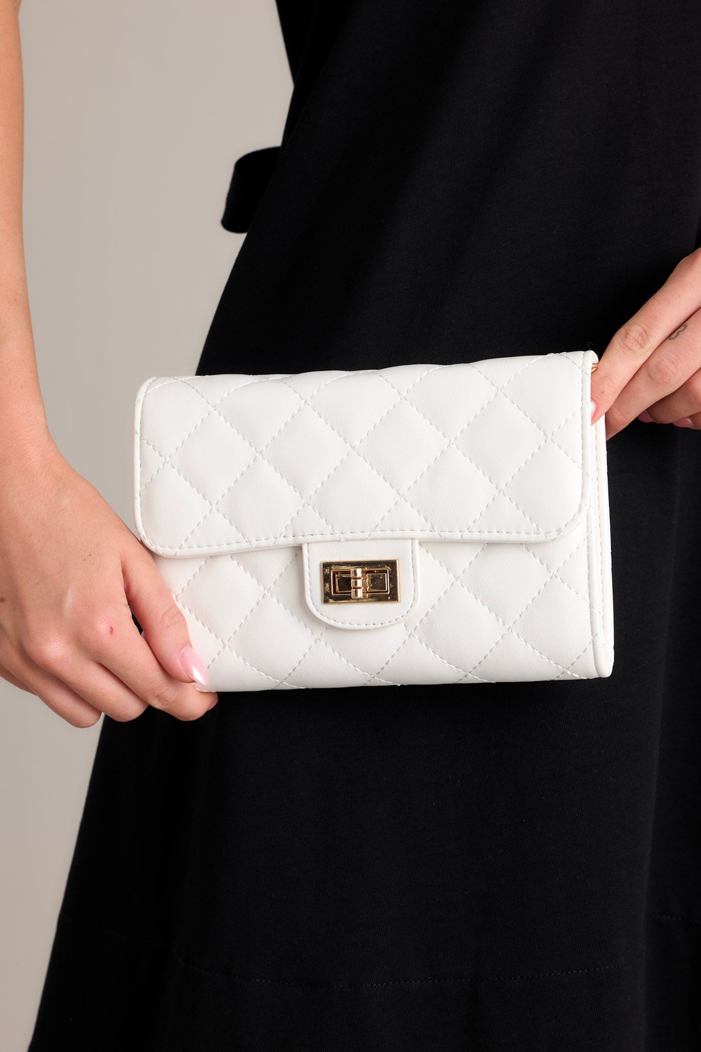 Close-up view of this white bag that features gold hardware, a quilted design, turn lock closure, a zipper pocket inside, and a detachable chain shoulder strap. 