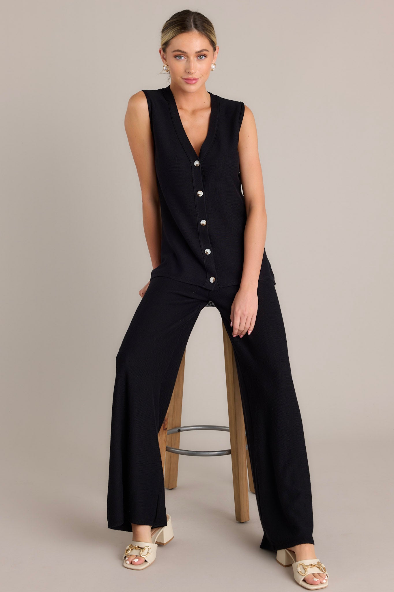 Seated, full body view of these black pants featuring a high waisted design, a thick elastic waistband, a soft knit material, and a wide leg.