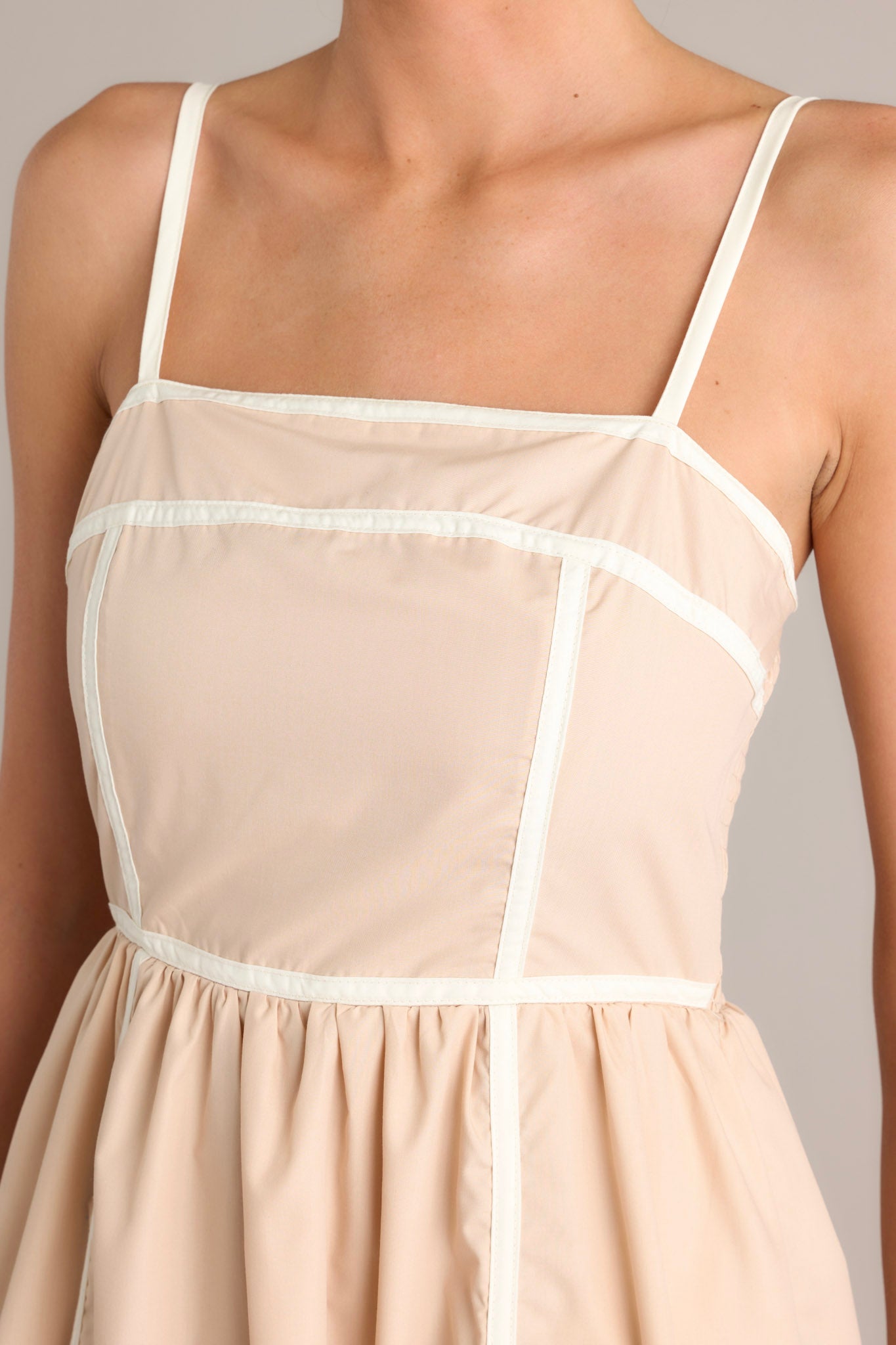 Close-up of the beige maxi dress showing the square neckline, thin adjustable straps, and thick contrasting seams.