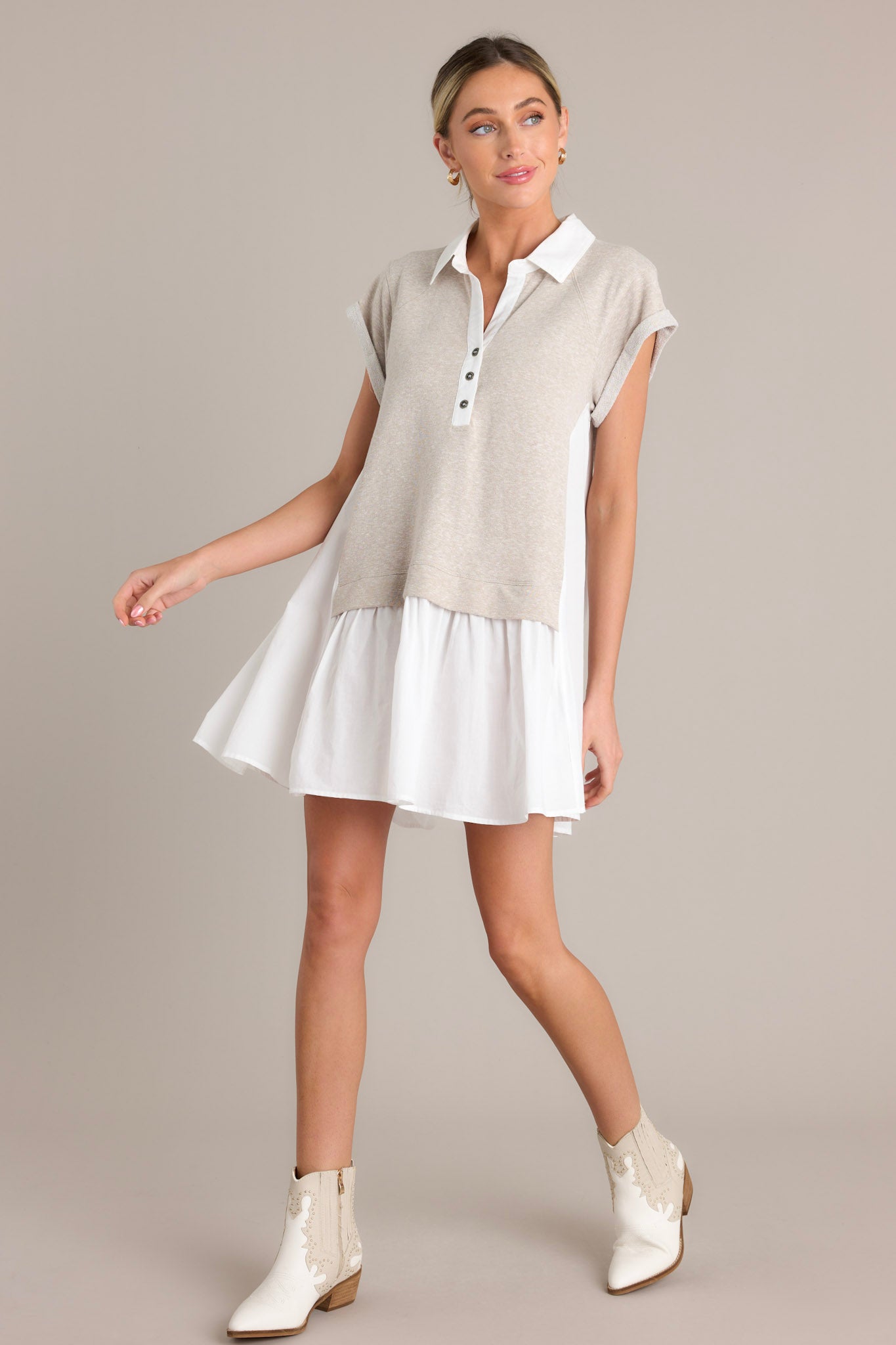 Action shot of a taupe mini dress displaying the flow and movement of the fabric, highlighting the collared v-neckline, functional chest buttons, attached sweater overlay, and cuffed short sleeves.