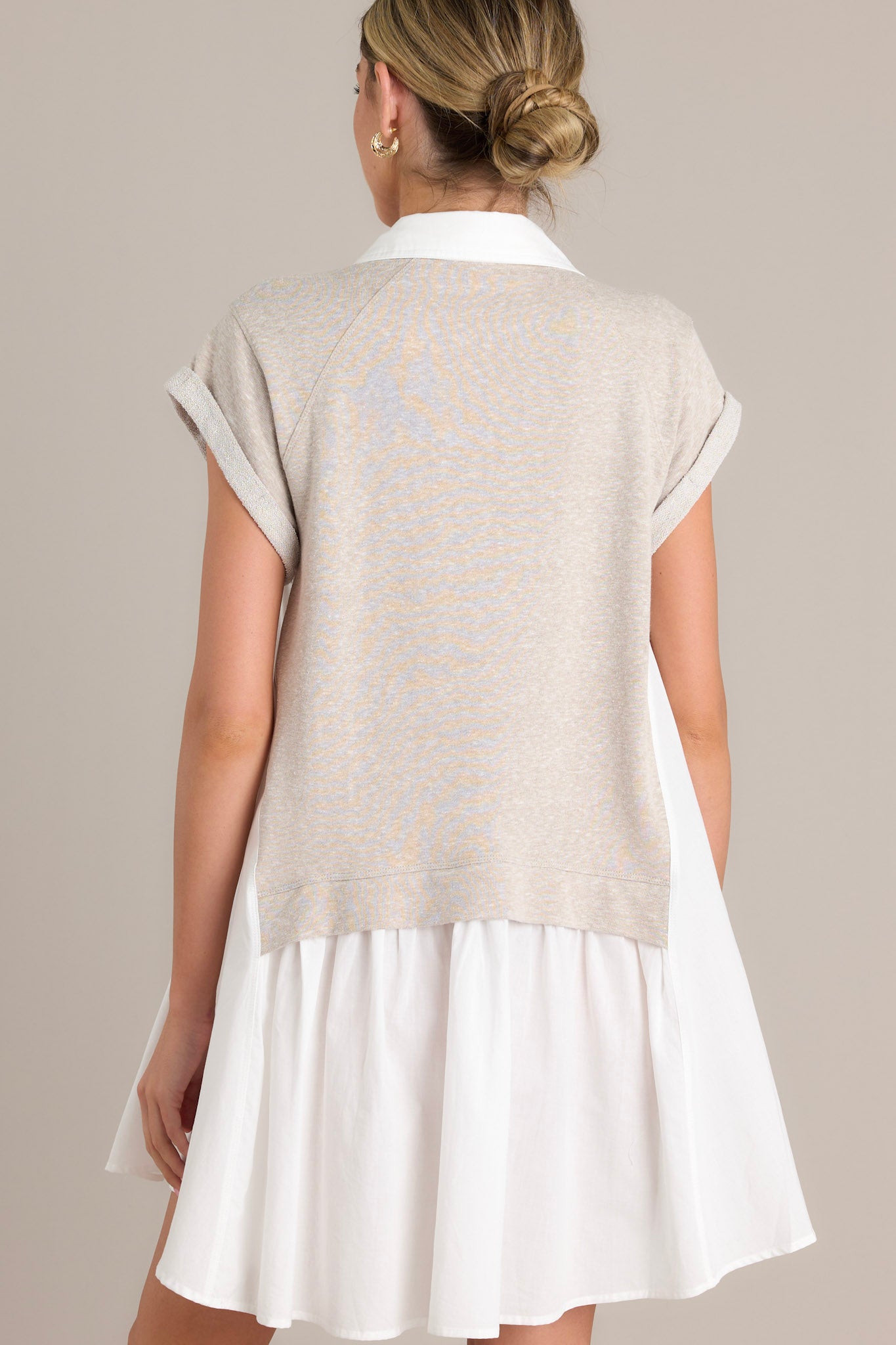 Back view of a taupe mini dress highlighting the attached sweater overlay and cuffed short sleeves.