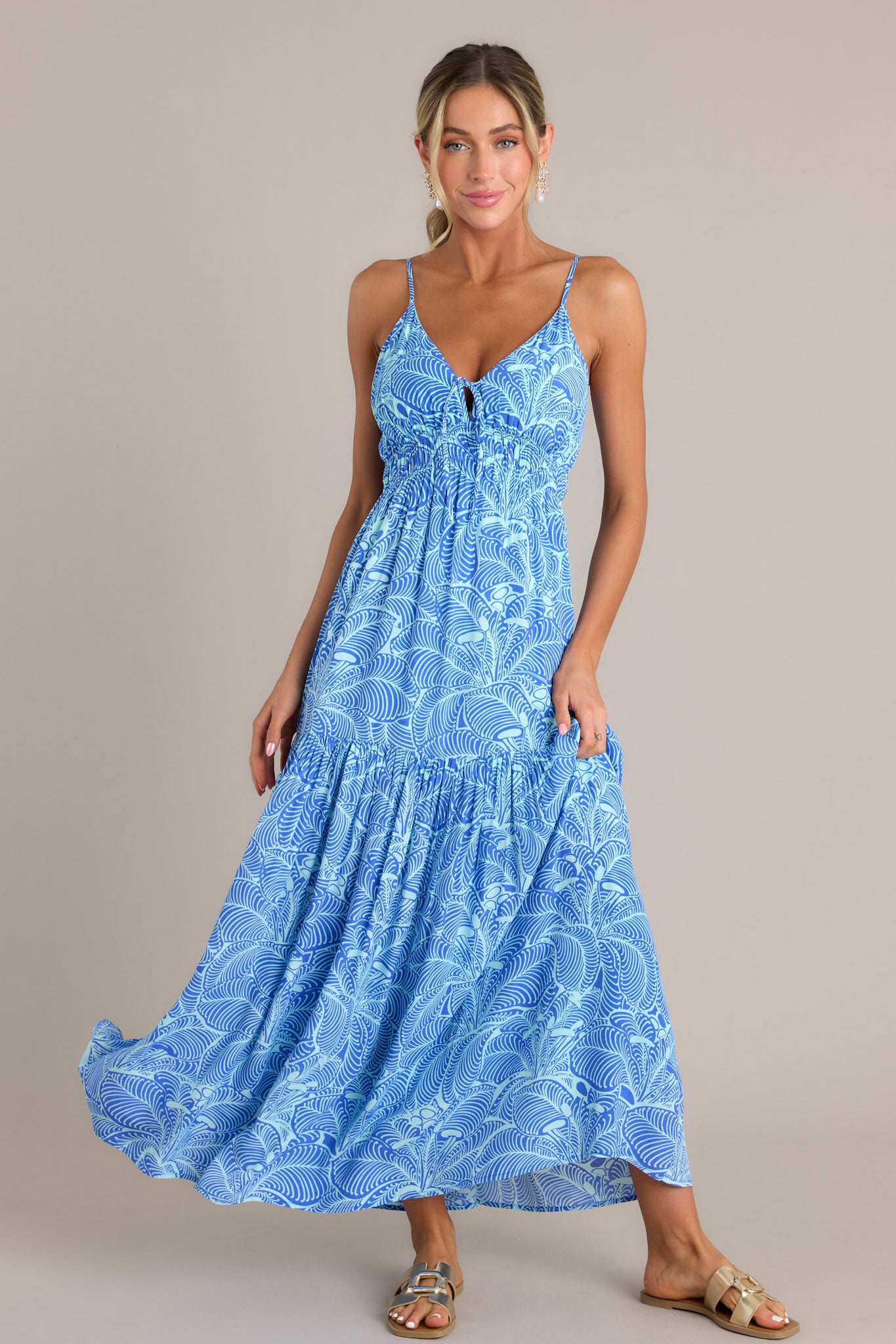 The blue maxi dress showcases a v-neckline with thin adjustable straps, a self-tie detail at the bust, and a flowy tiered skirt.