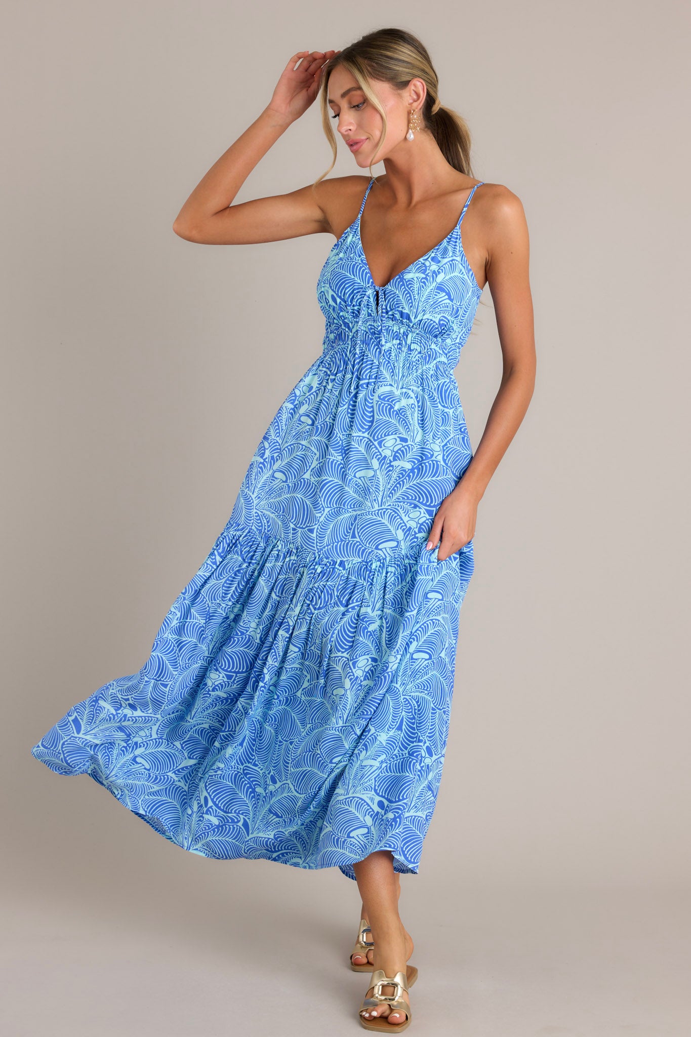 A blue maxi dress with a v-neckline, thin adjustable straps, self-tie bust, elastic waistband, and a single tier creating a flowing silhouette.