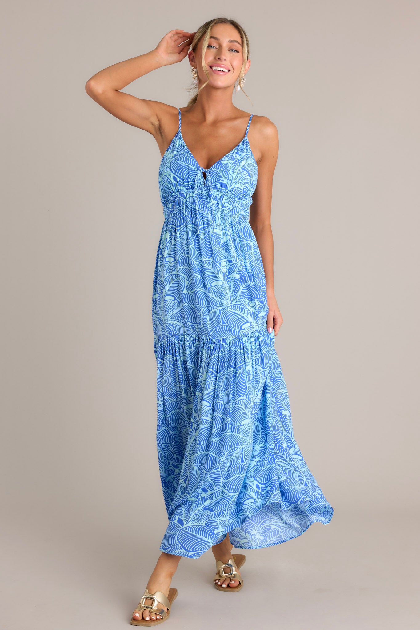 This blue maxi dress has a v-neckline, thin adjustable straps, a self-tie detail at the bust, an elastic waistband, and a single tier for a flowing look.