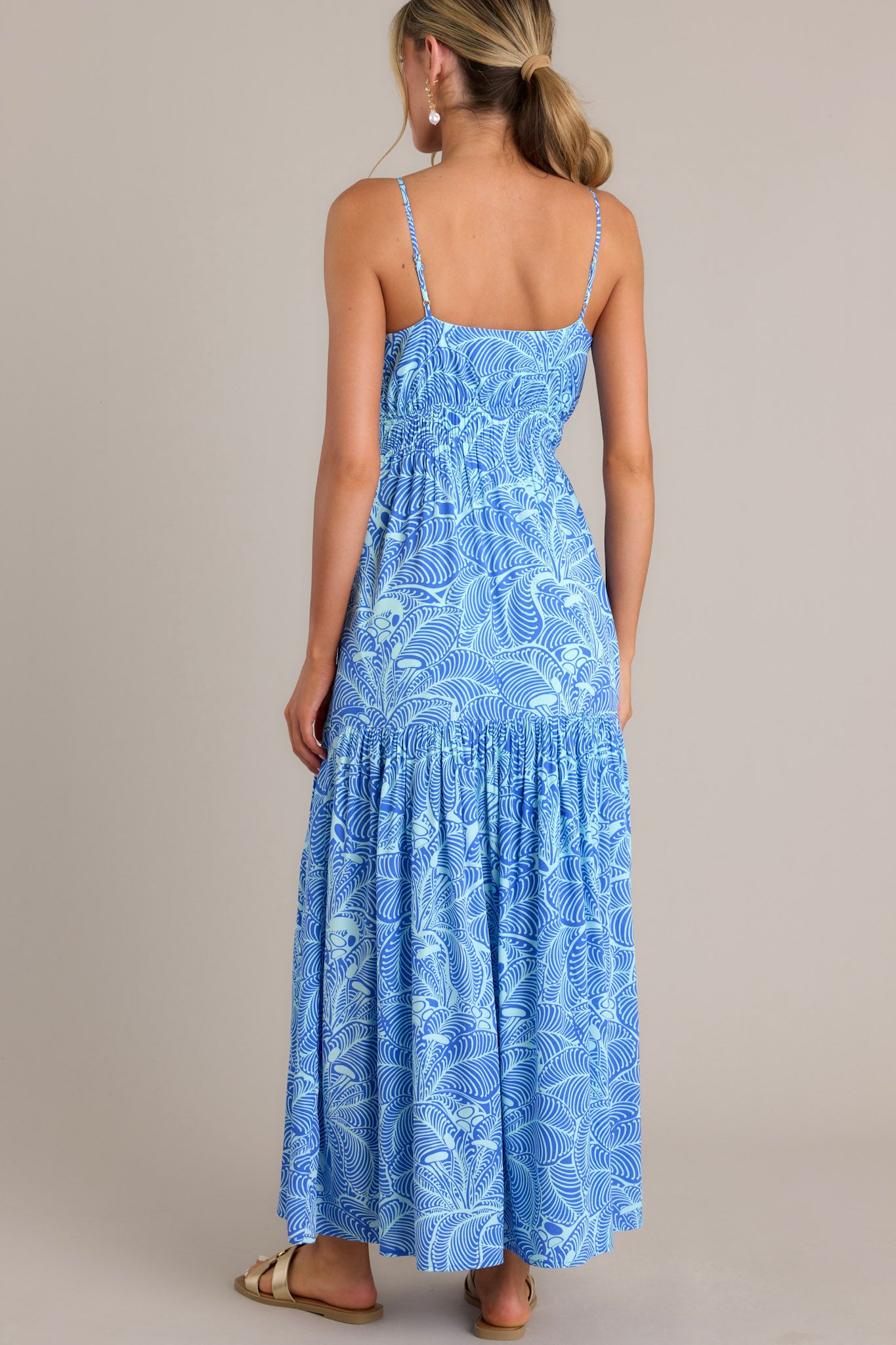 The back of the blue maxi dress shows thin adjustable straps, an elastic waistband, and the flowing tiered skirt.