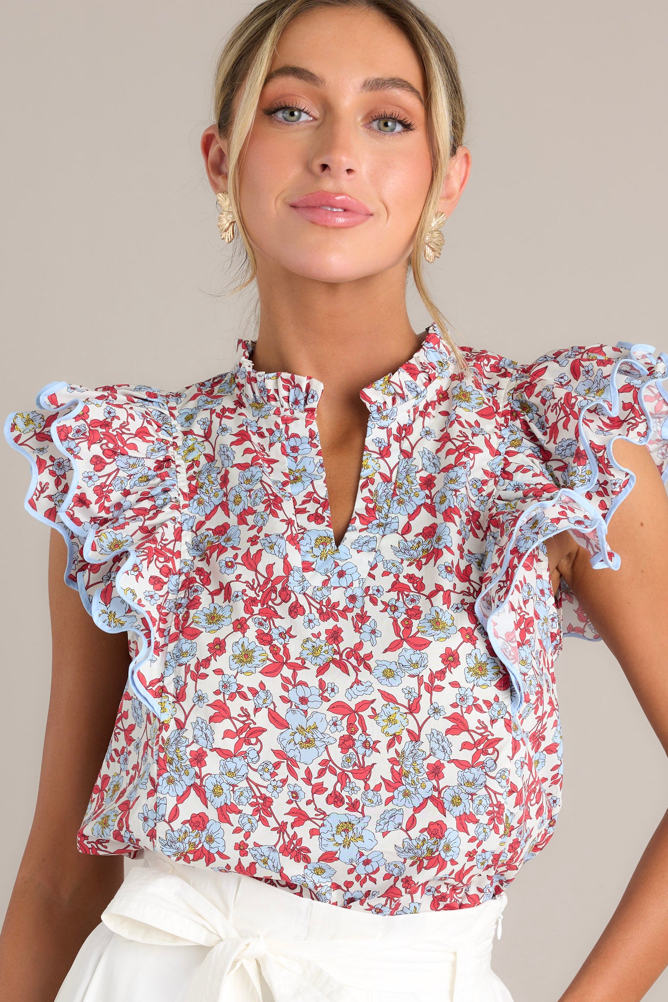 This red top features a ruffled v-neckline, a red & light blue floral print, and ruffled short sleeves with ricrac detailing.