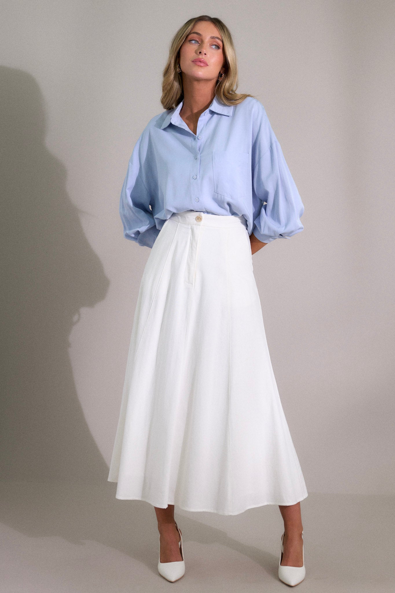 This ivory midi skirt features a high waisted design, a button & zipper closure, functional hip pockets, visible front & back seams, and a flowing silhouette.