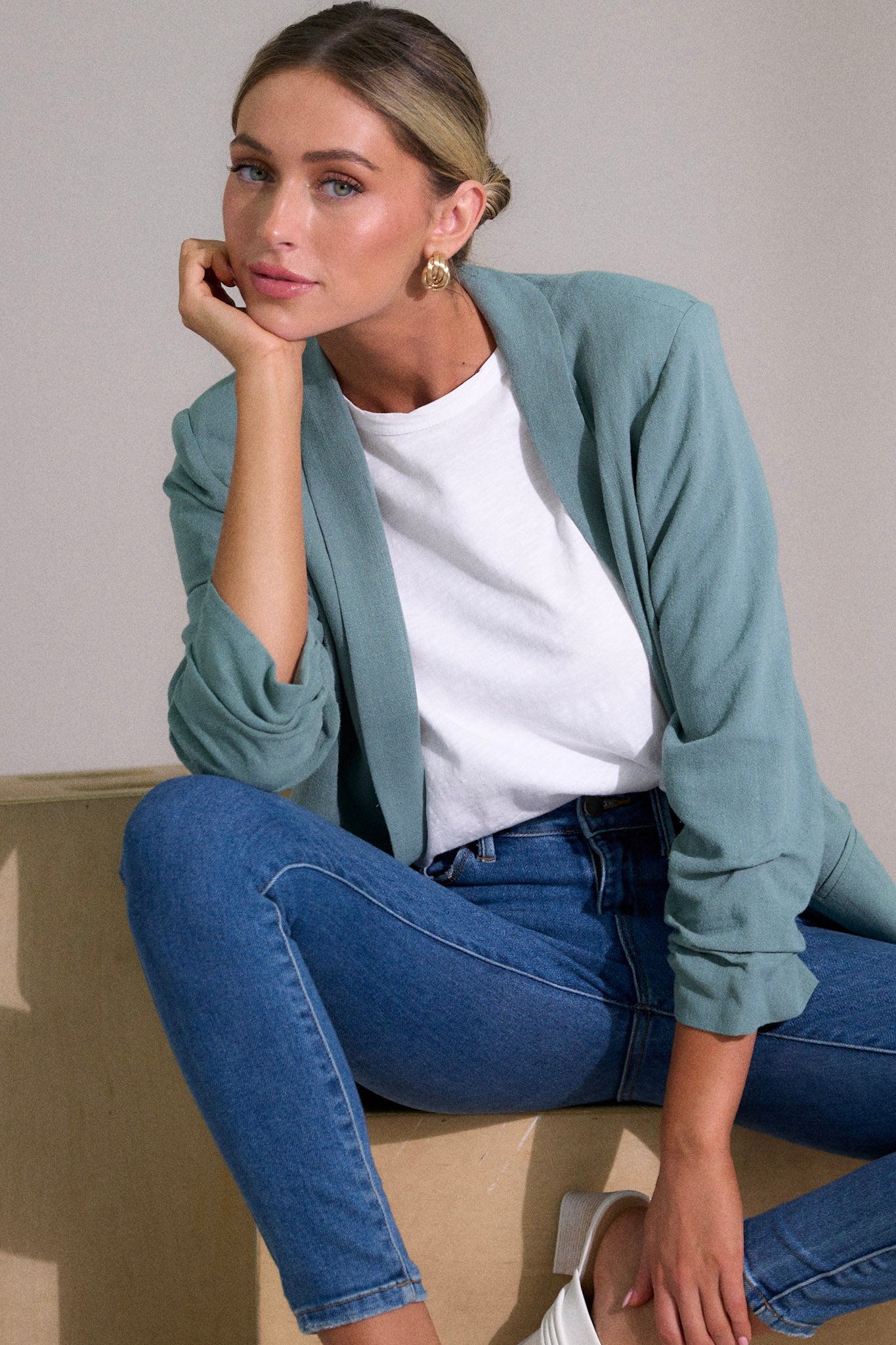 Front angled view of a blazer featuring a folded neckline, shoulder padding, faux pockets, and gathering in the quarter length sleeves