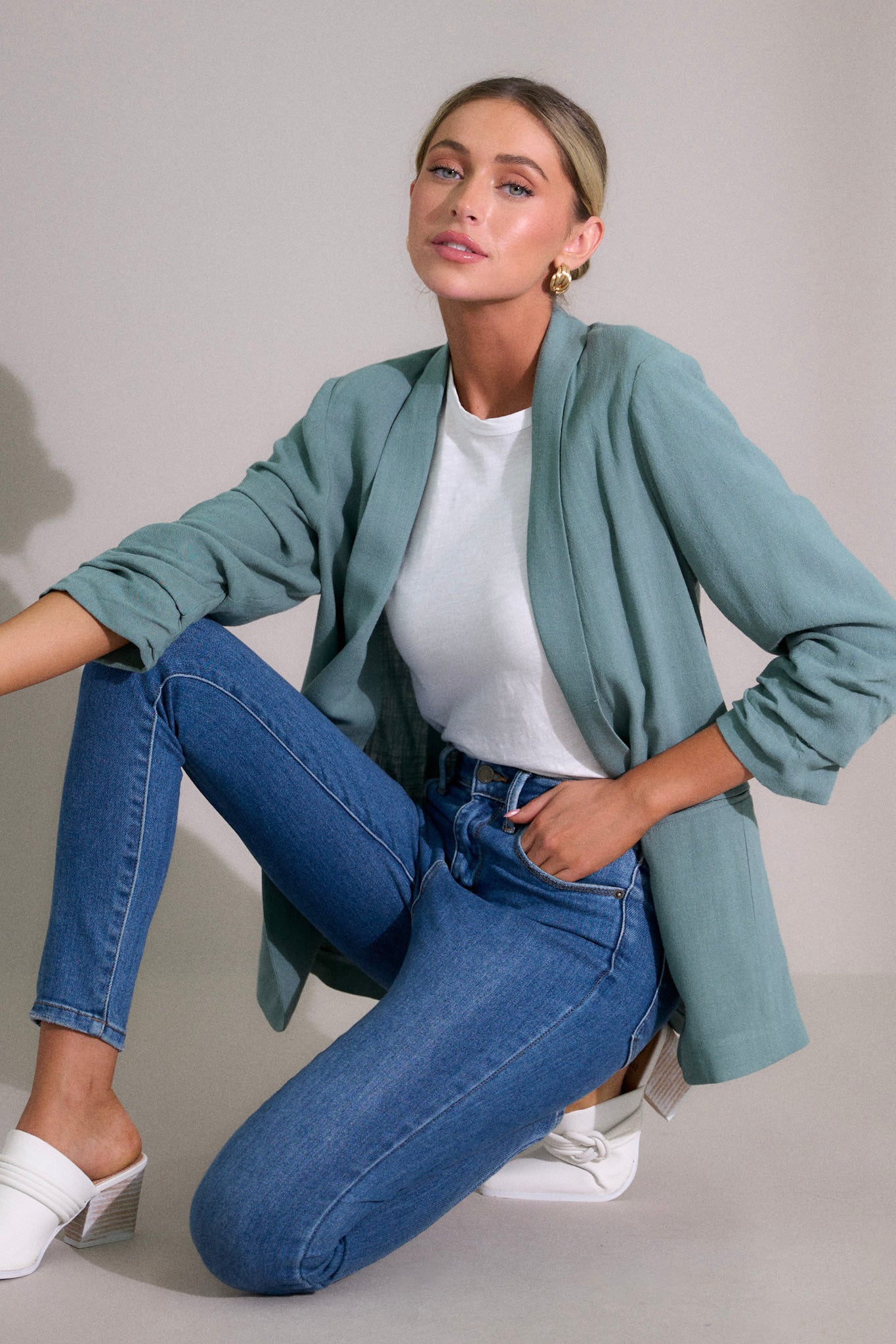 This blazer features a folded neckline, shoulder padding, faux pockets, and gathering in the quarter length sleeves.