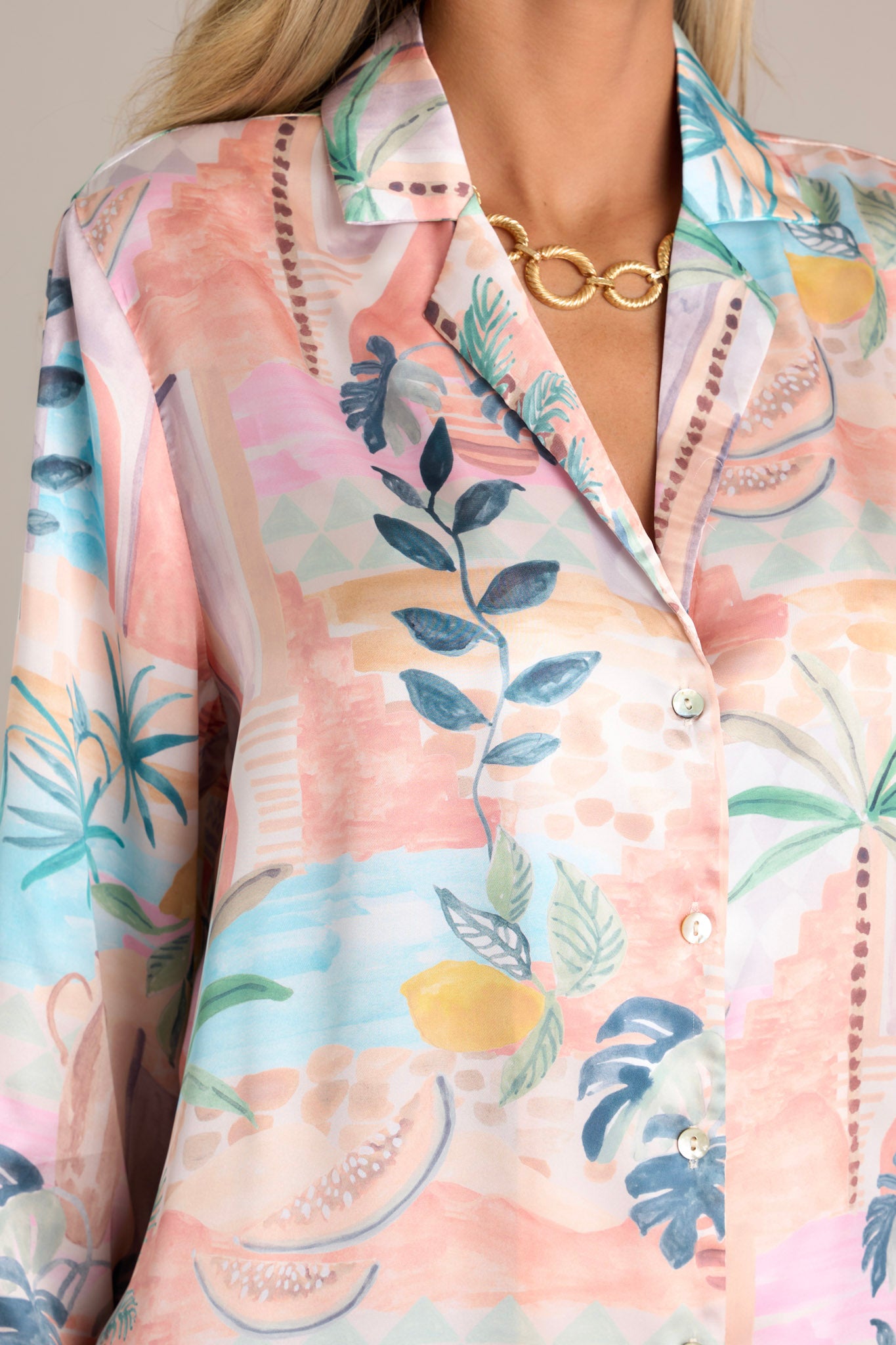 Close-up of the notched lapel collared neckline, functional button front, and button cuffed long sleeves on a peach top with a split hemline.