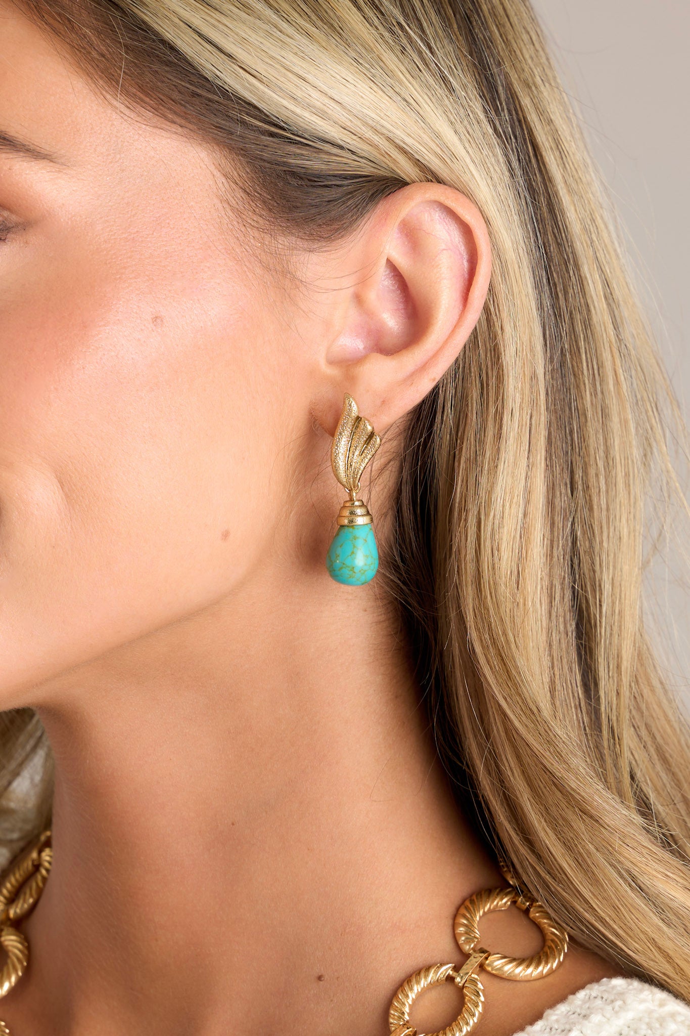 These gold earrings feature textured winged studs, a turquoise stone drop pendant, and secure post backings.