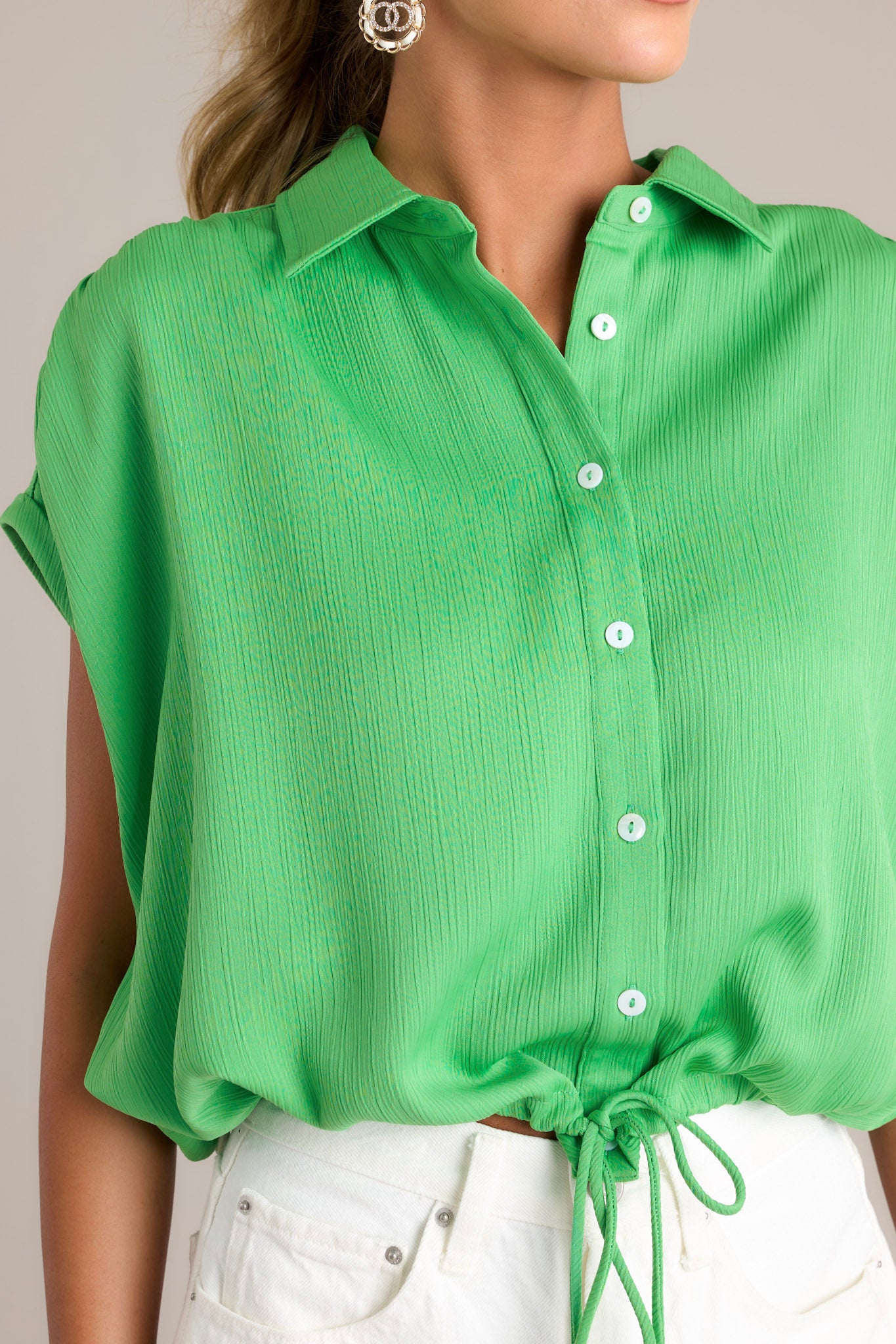 Close-up of the green top showing the collared neckline, functional button front, and self-tie drawstring hemline.