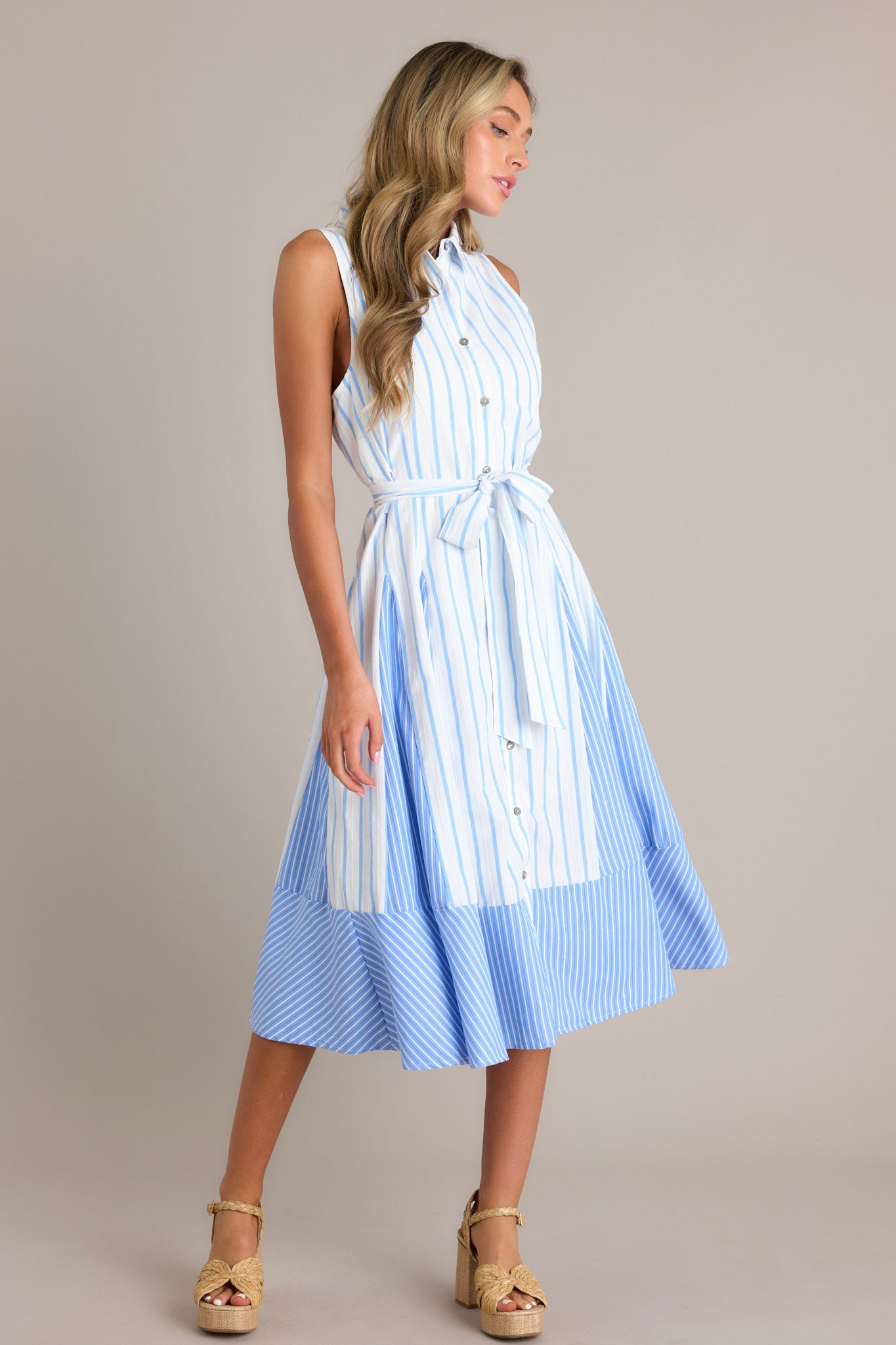 Side view of a light blue midi dress showcasing the collared neckline, functional button front, self-tie waist belt, unique stripe pattern, and flowing silhouette.