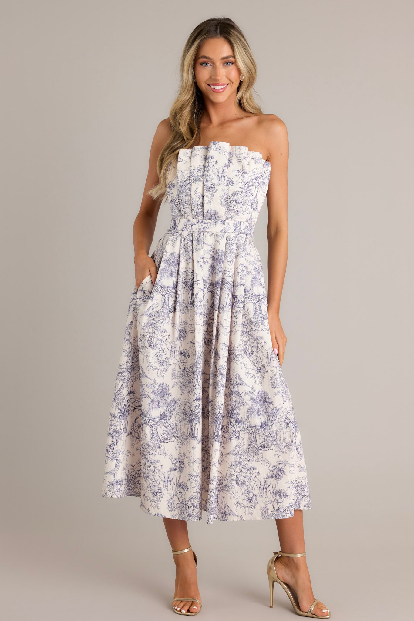 Full view of this blue toile strapless midi dress with a structured, pleated bodice, functional pockets, and a smocked back.