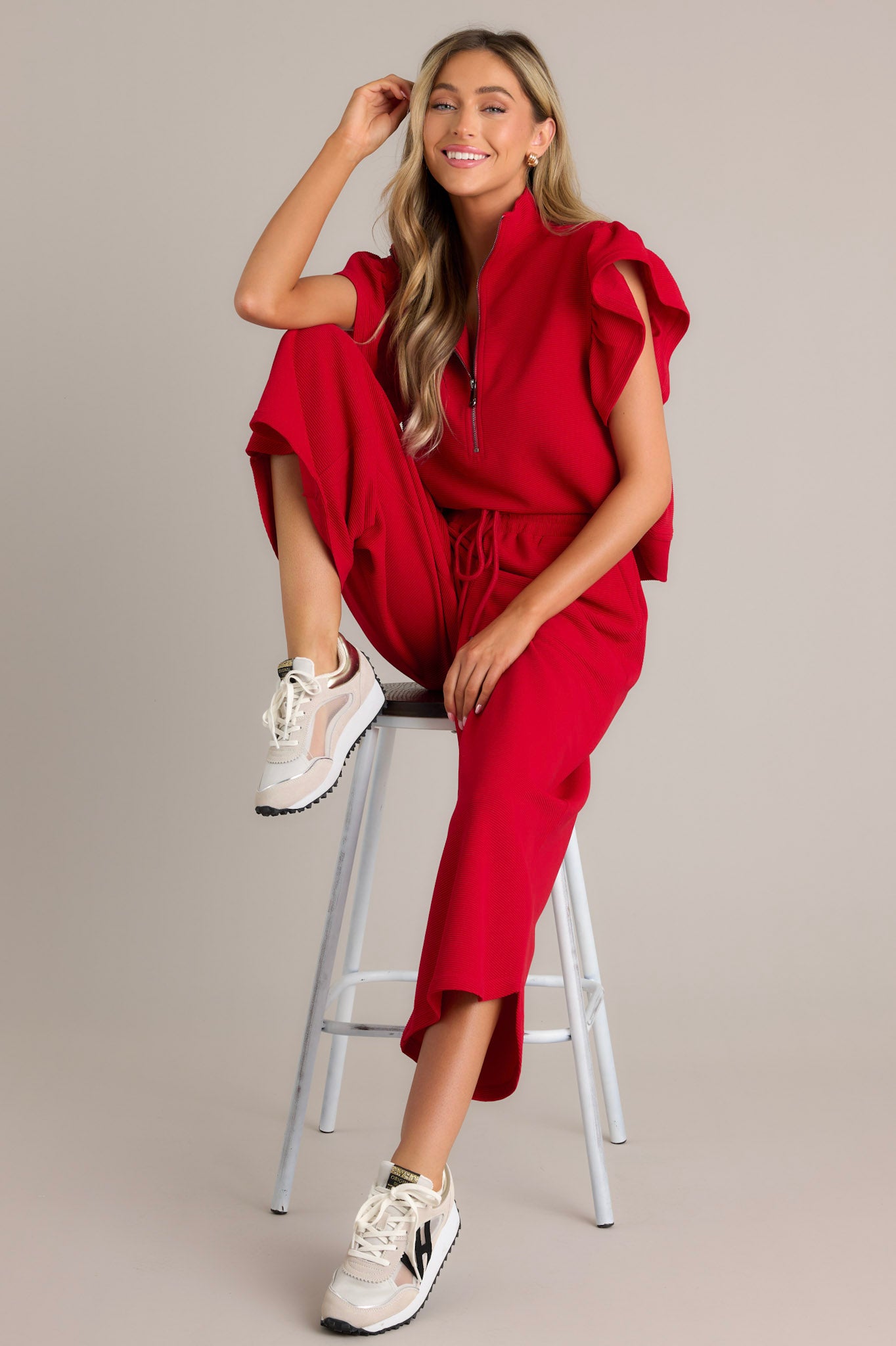 These red pants feature a high waisted design, an elastic waistband, a self-tie drawstring, functional hip pockets, a ribbed texture, a wide leg, and a scooped hemline.