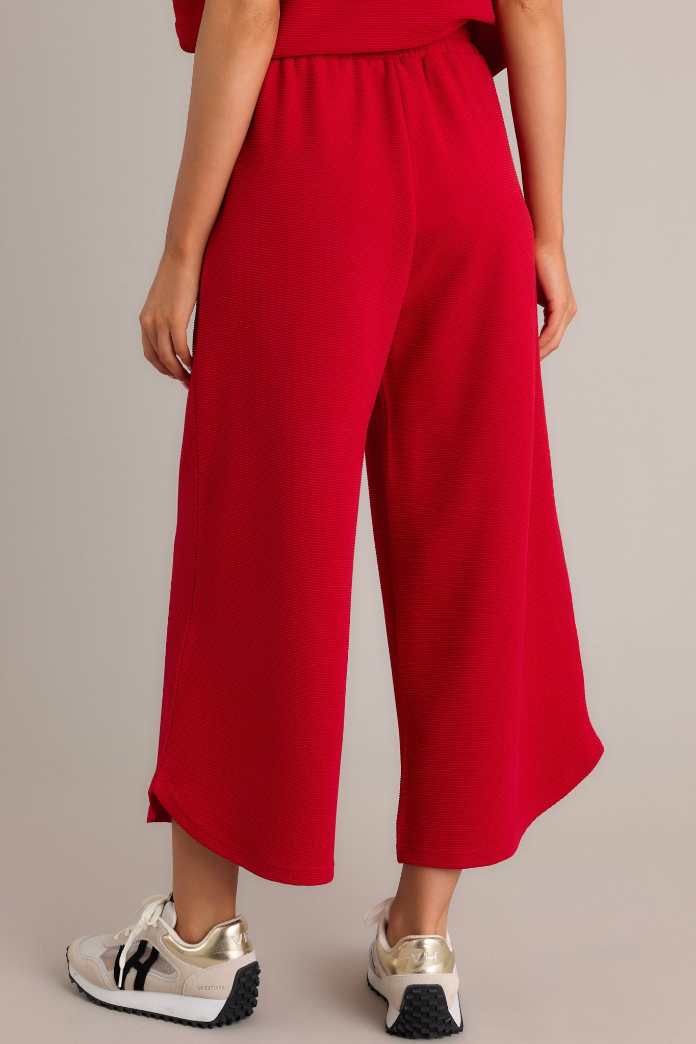 Back view of red pants featuring the high waisted design, ribbed texture, functional hip pockets, and a scooped hemline.